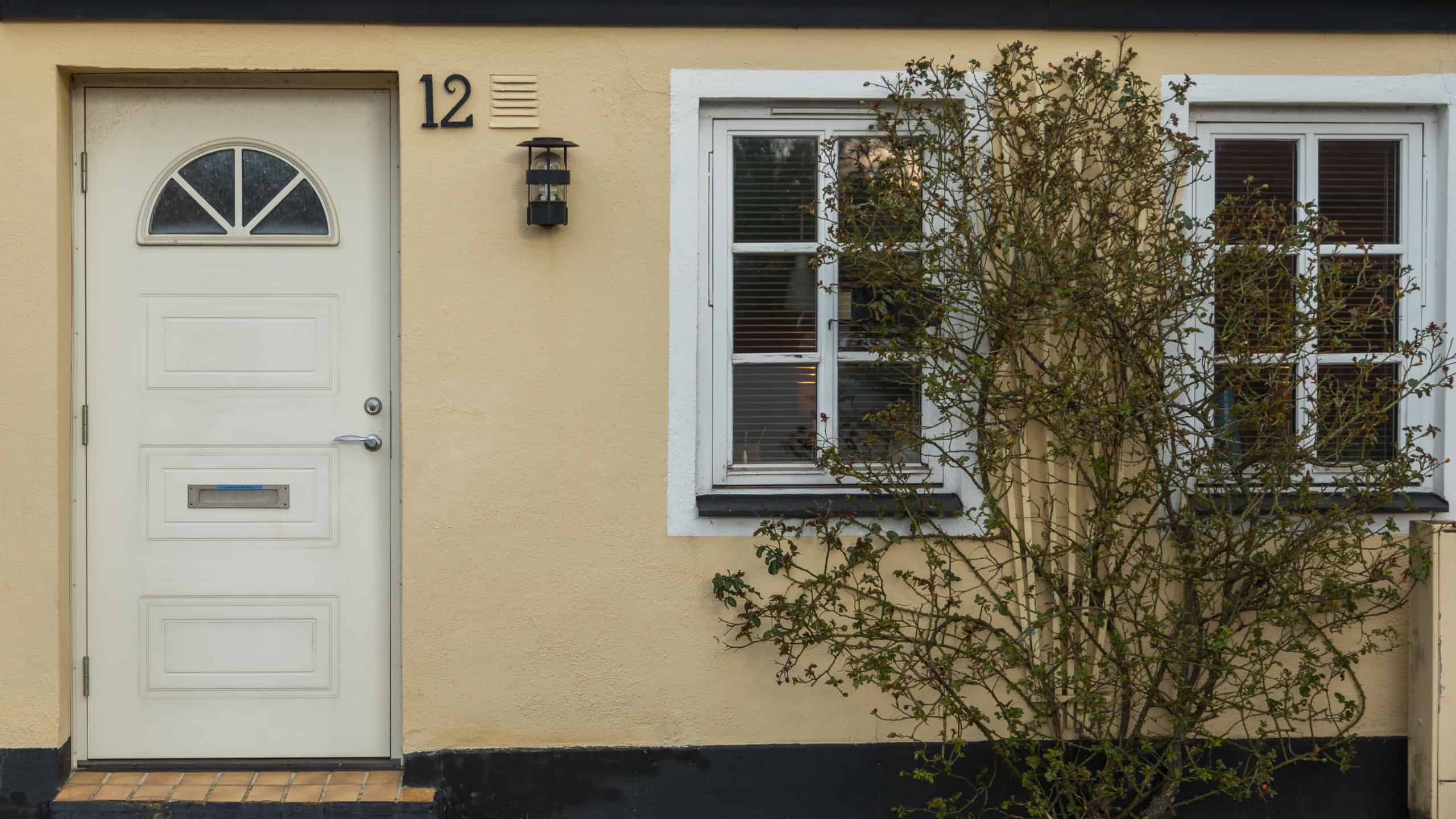 Simple yellow house front with white door, windows and a bare bush in Ystad, Sweden.