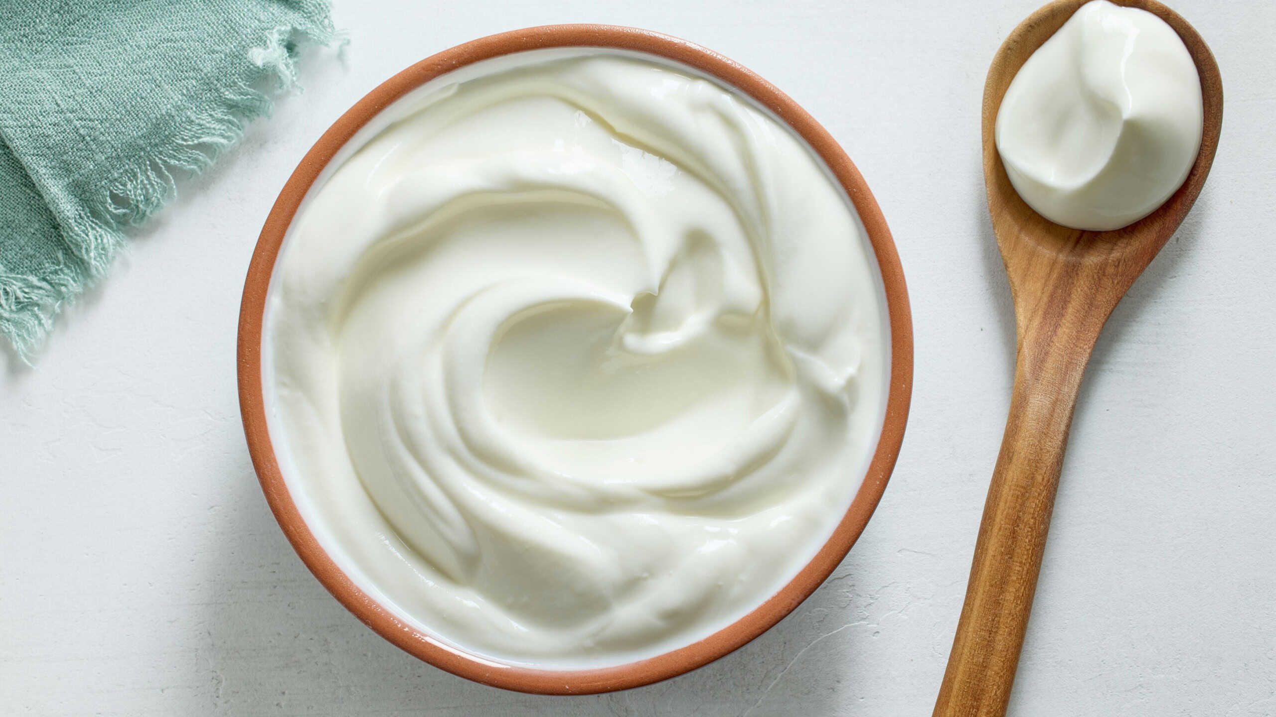 Bowl of sour cream yogurt on white kitchen table, top view