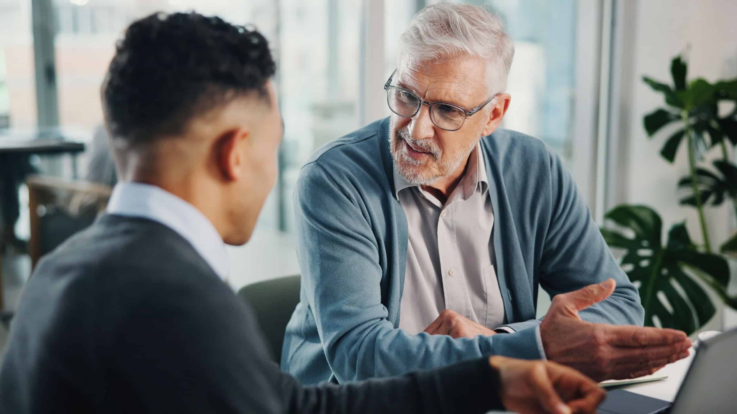 Question, senior man or financial advisor talking with laptop, retirement fund or pension info in conversation. Elderly client, office and people in meeting planning for future, advice or consulting