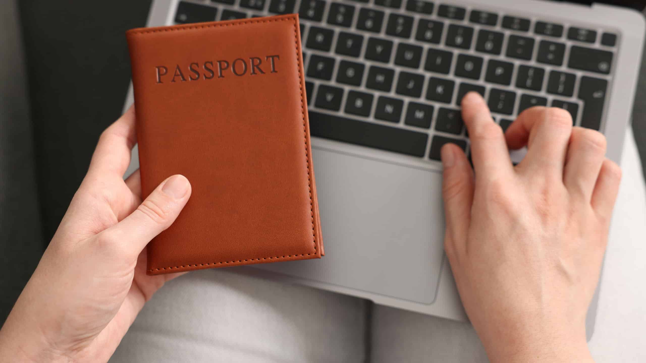 Woman with passport using laptop indoors, above view