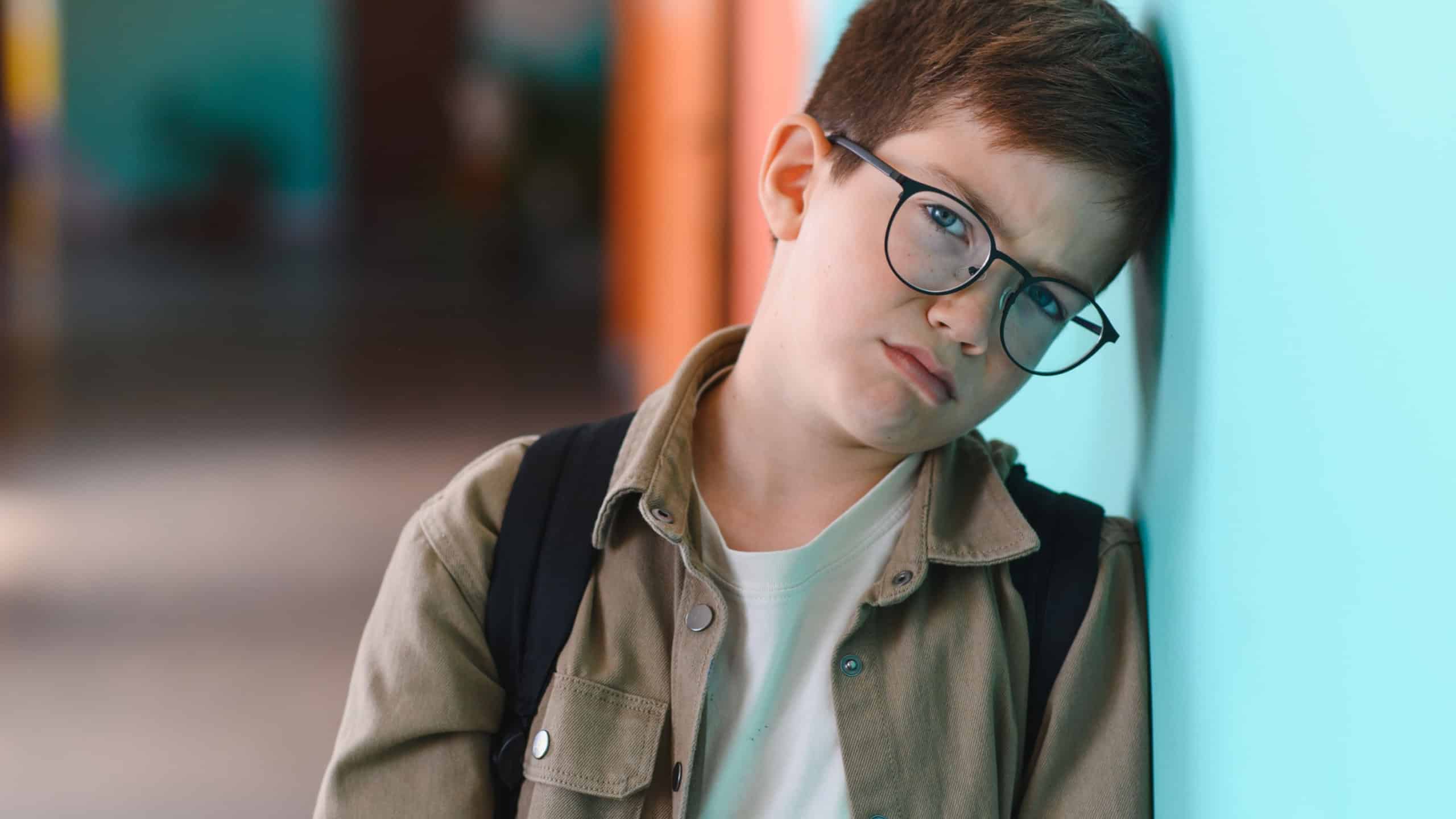 Sad schoolboy leaning against a wall in a school corridor, crying and feeling the weight of bullying from classmates, experiencing deep emotional distress