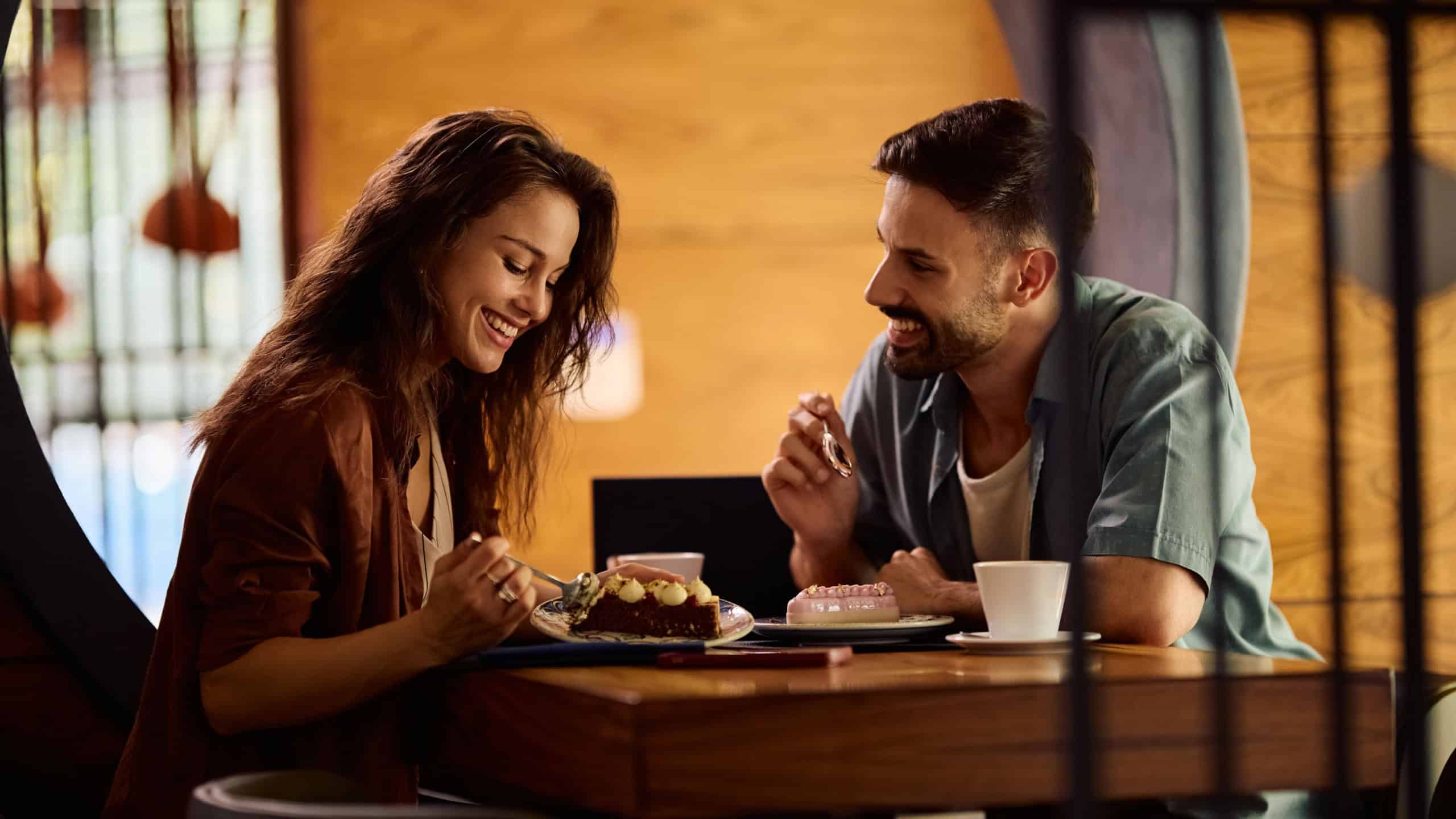 Happy couple talking to each other while eating dessert on a date in a cafe.