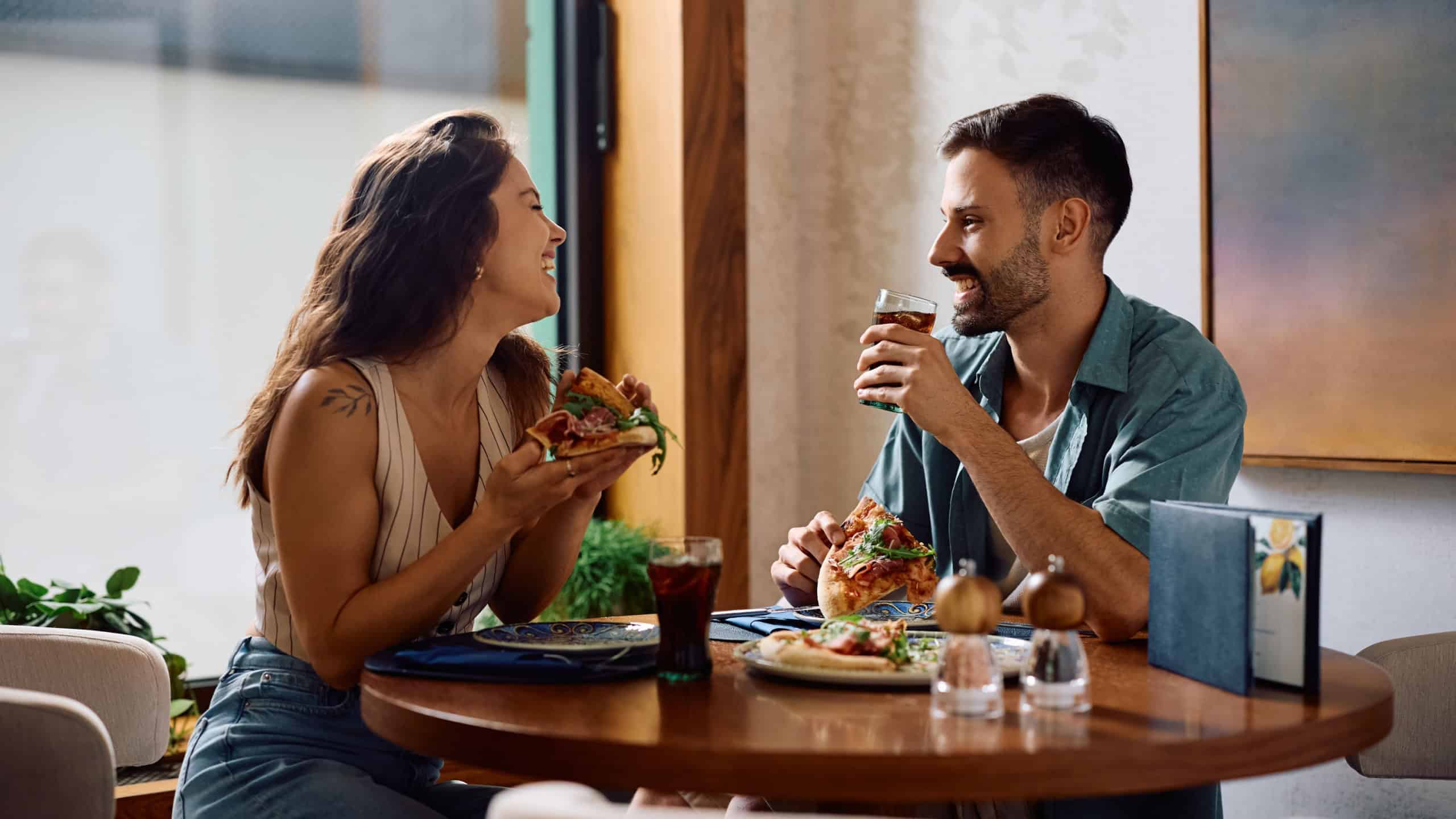 Young happy couple eating pizza and talking in a restaurant.