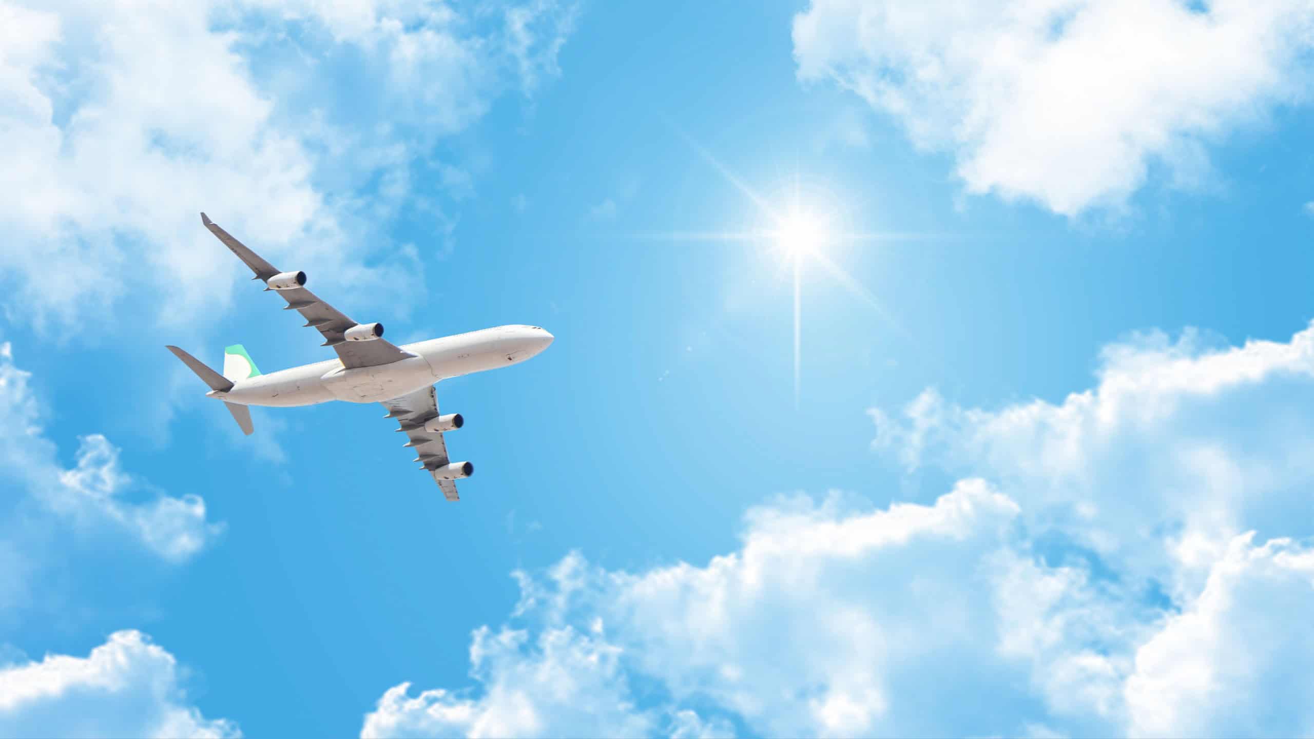Passenger plane flying in sunny sky. Airplane, white clouds and bright summer sun in the beautiful blue sky.