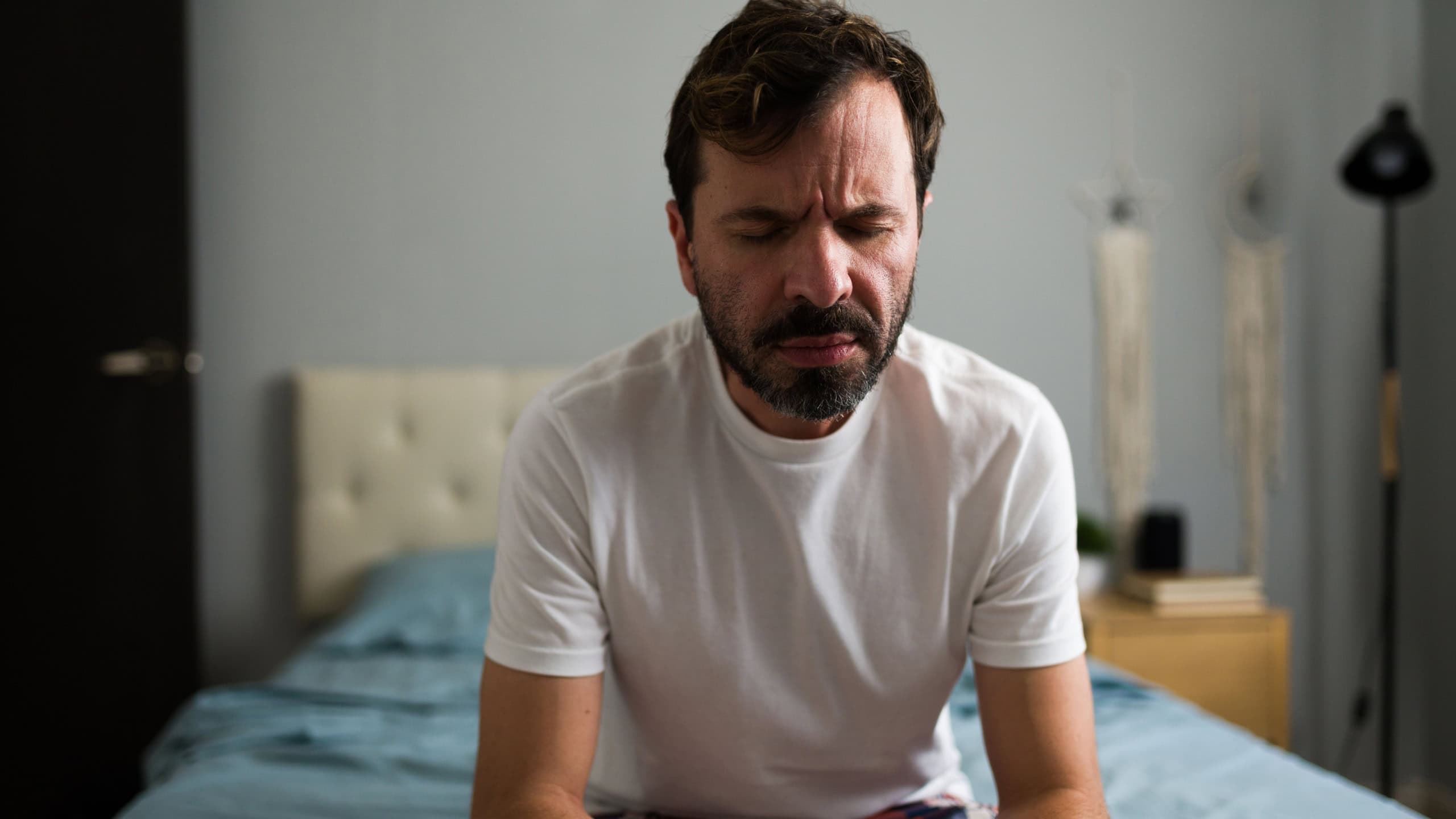 Unloved man sitting on bed with eyes closed, experiencing grief and loneliness after relationship breakup