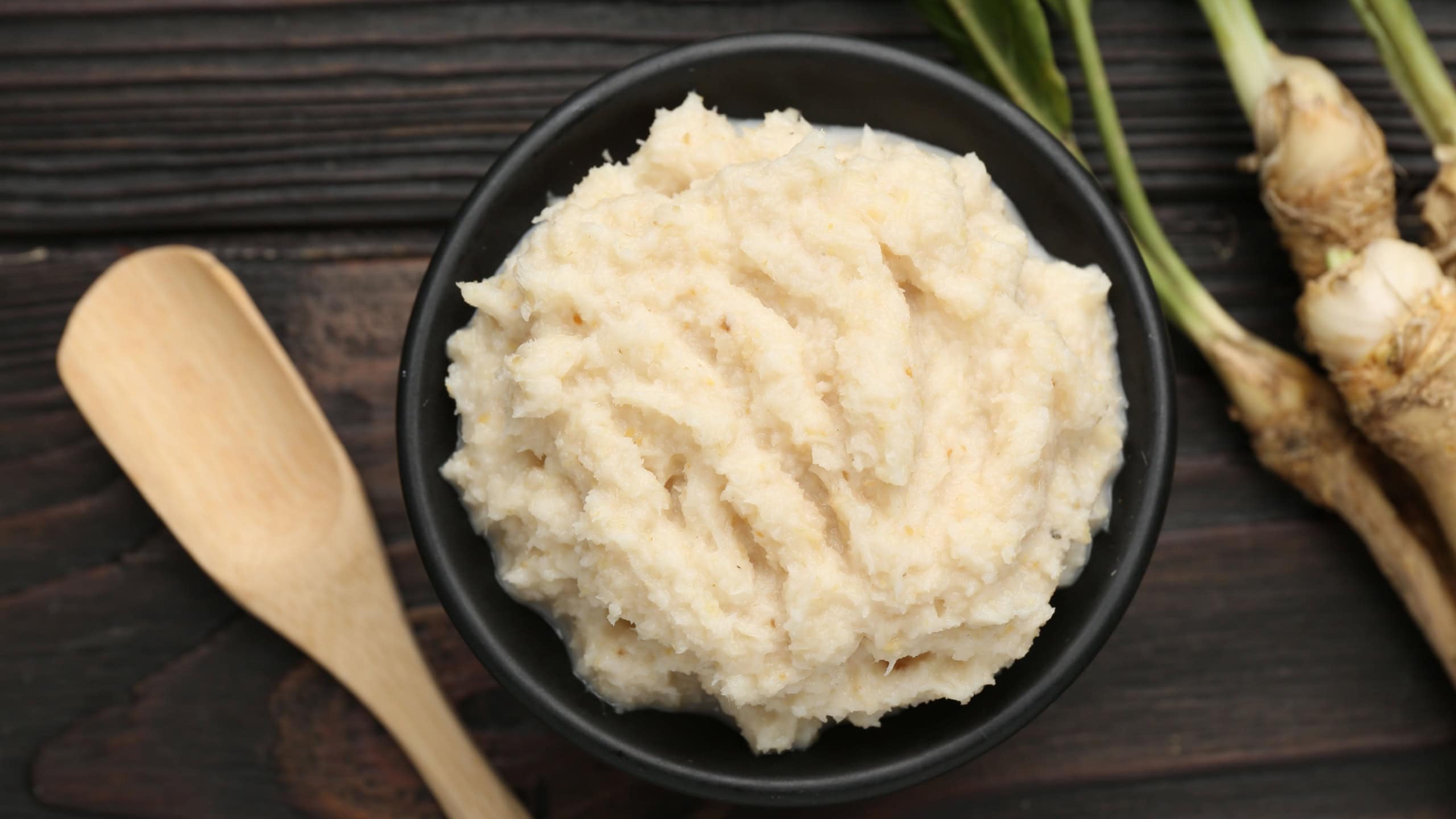 Tasty horseradish sauce and roots on black wooden table, flat lay