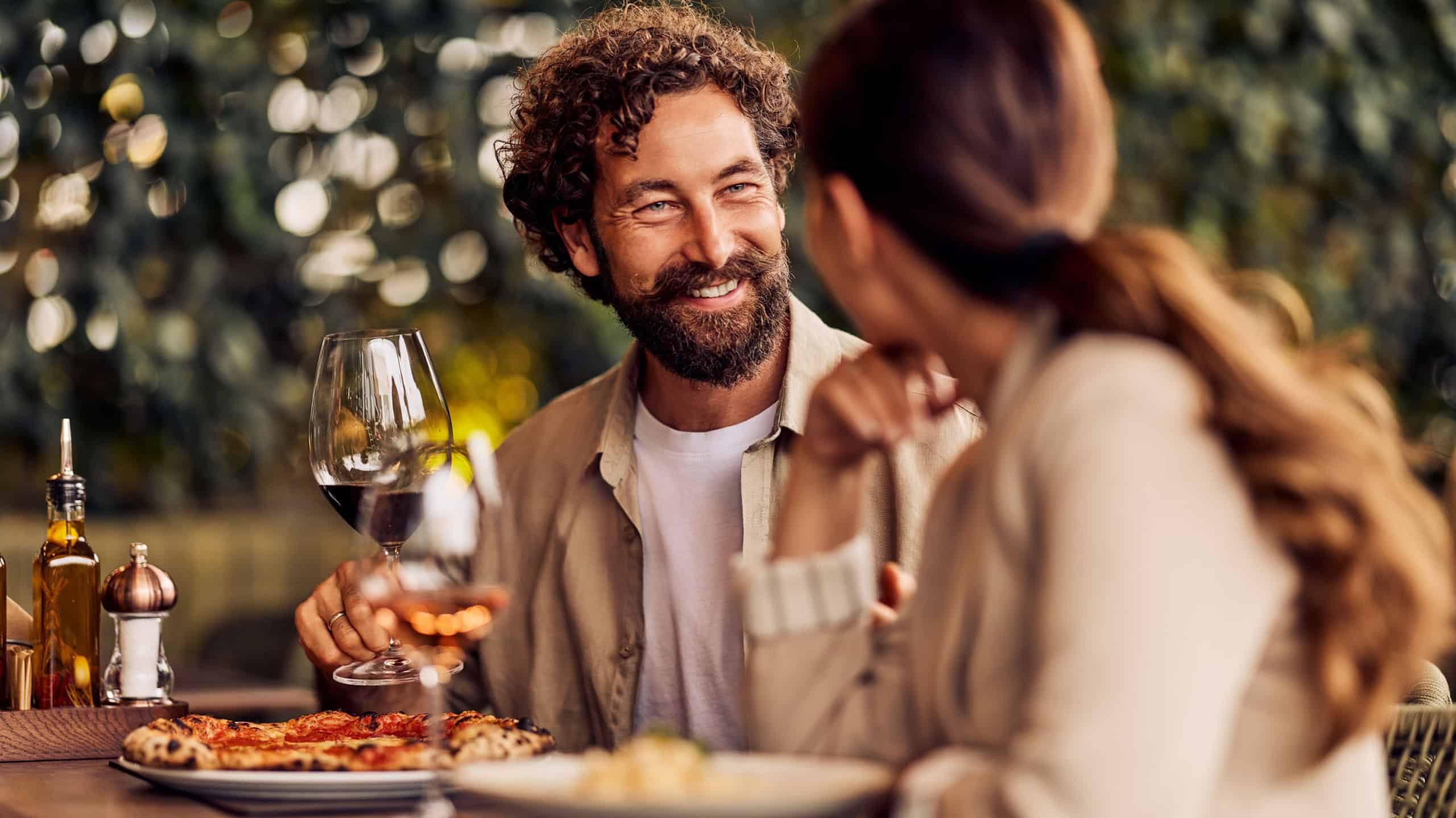 Couple enjoying a romantic meal outdoors, laughing while sharing wine and good conversation.