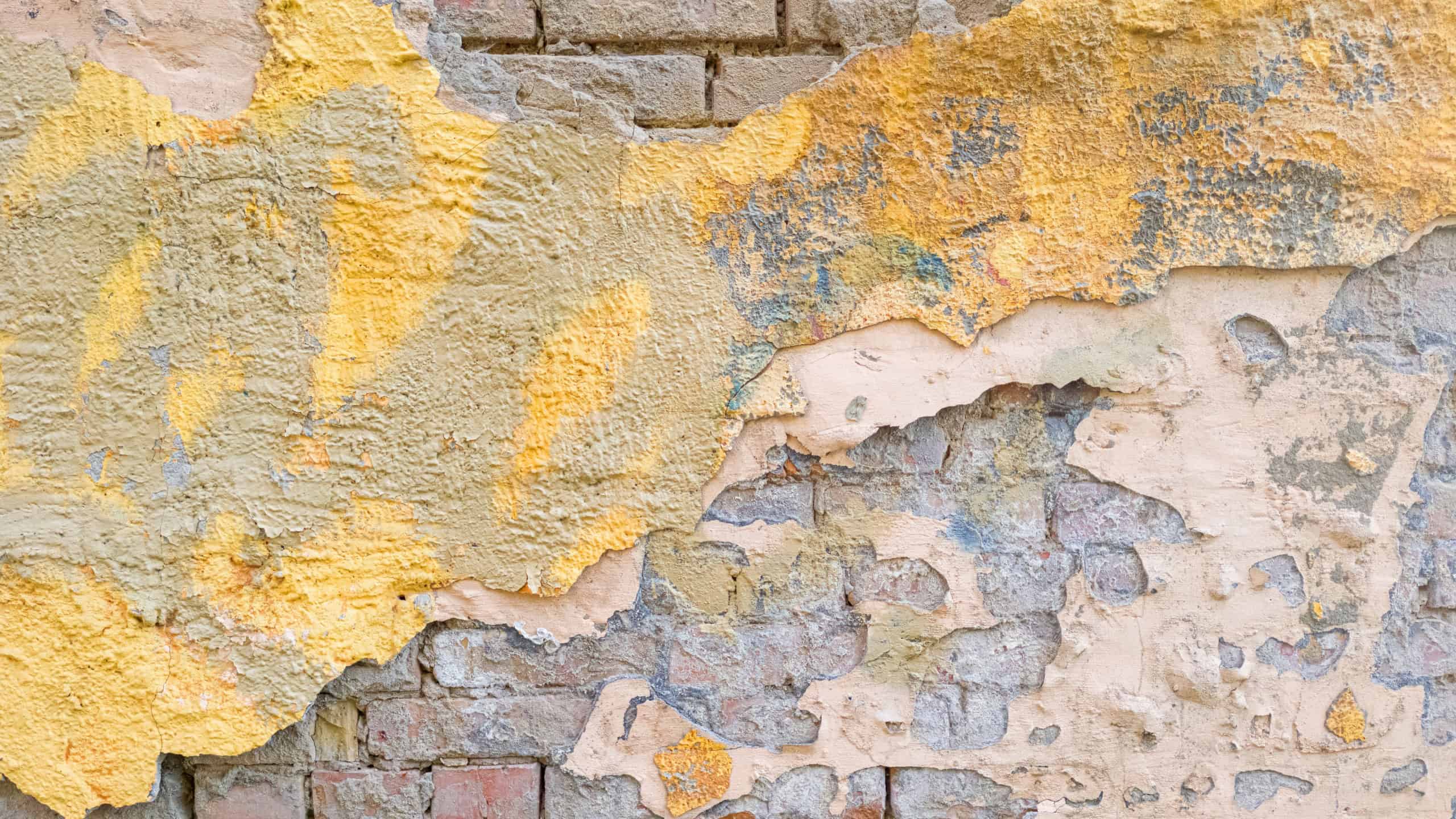 An old brick wall with peeling plaster and paint layers offers a rustic texture. Its weathered look suits various design projects.