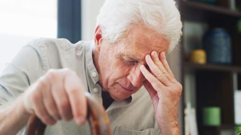 Headache, thinking and old man in house with cane, fatigue or memory of past mistake in living room. Mental health, grief or senior person in home with walking stick, migraine or regret in retirement
