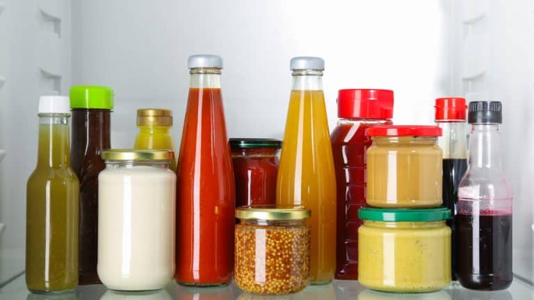 Bottles with different tasty sauces in fridge, closeup