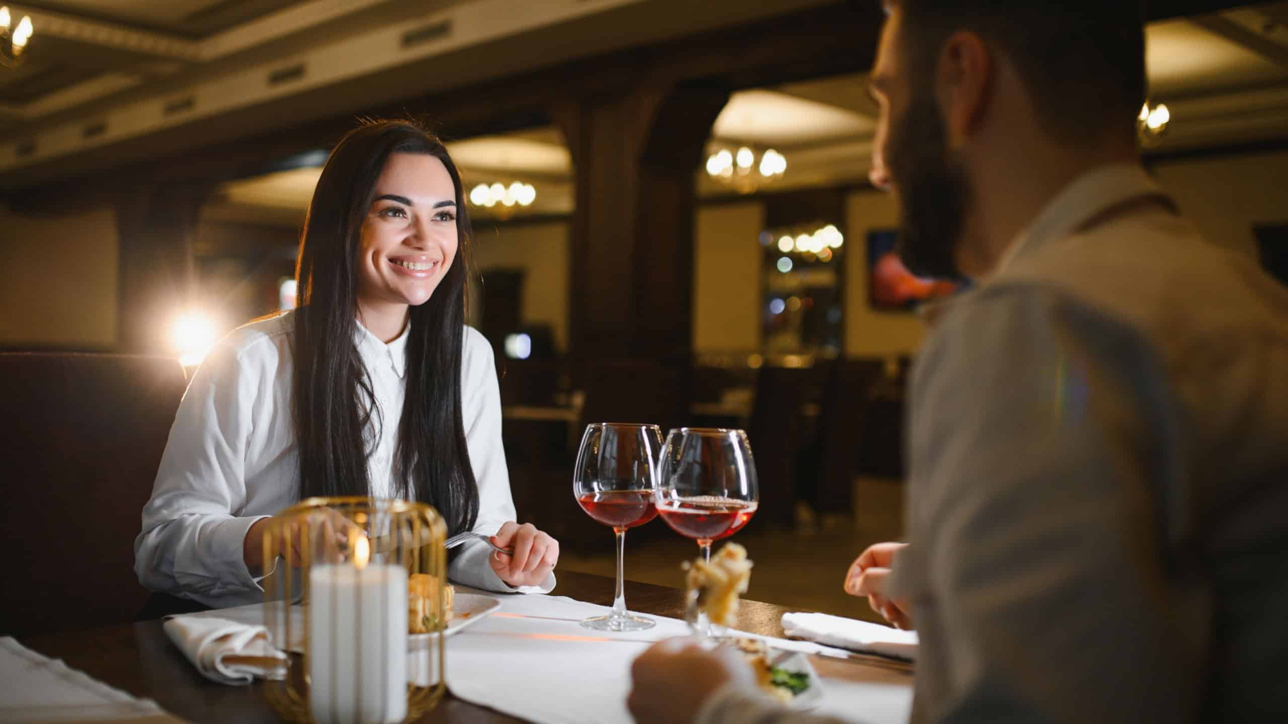 Young couple having a romantic dinner, smiling and talking at a restaurant. Two glasses of red wine on the table with a candle