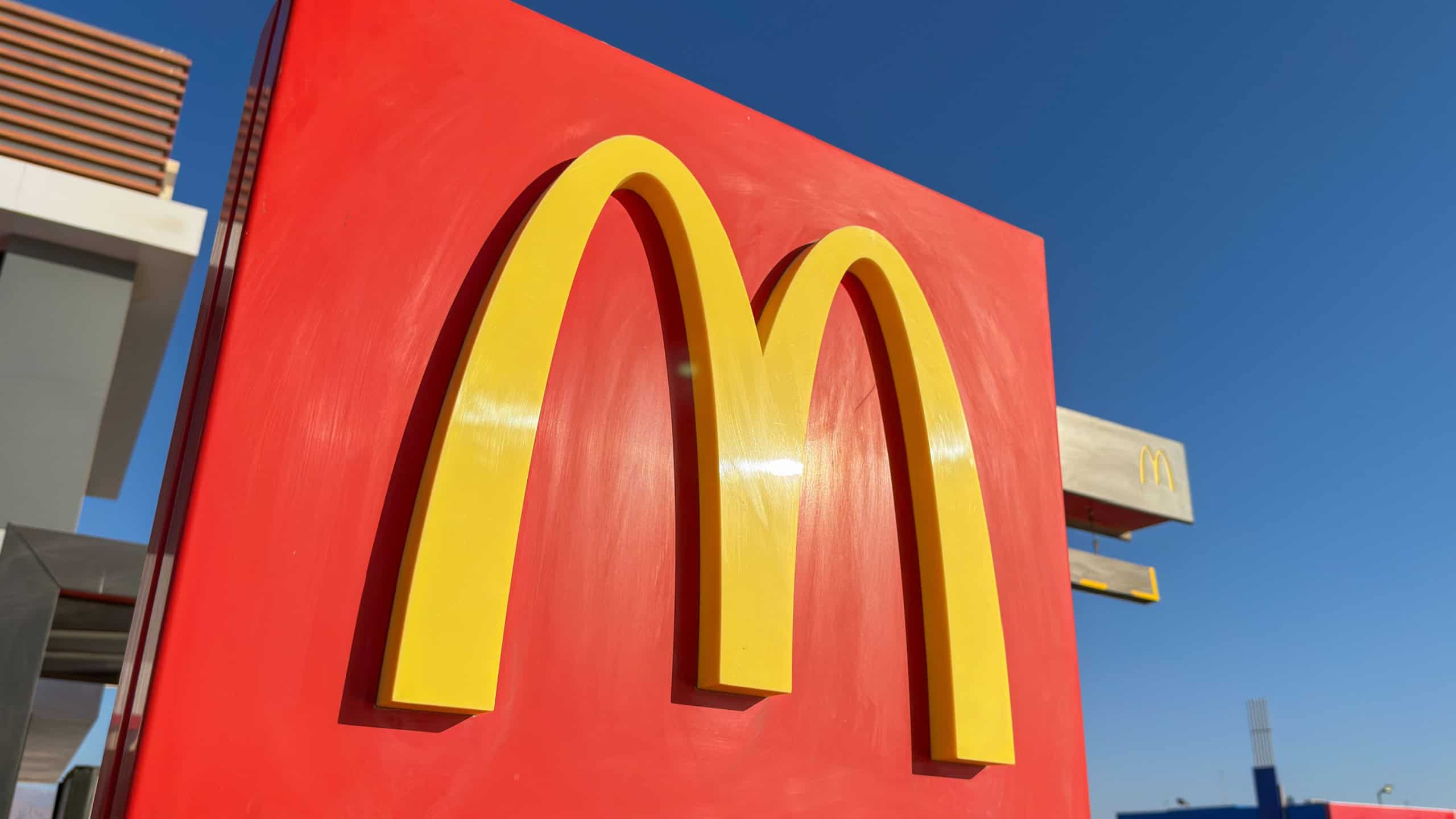 Close up of McDonalds golden arches logo on red sign against blue sky