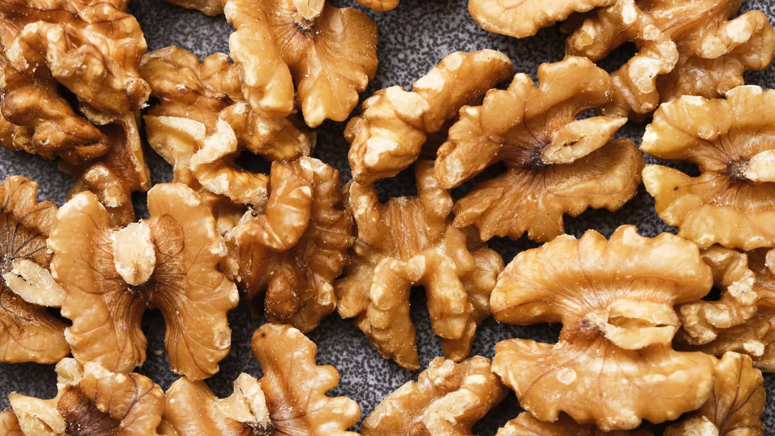 Walnut halves background texture. Shelled walnuts closeup view. Natural nut pattern filling frame. Healthy food ingredient concept. Raw brown walnuts surface. Organic snack backdrop.