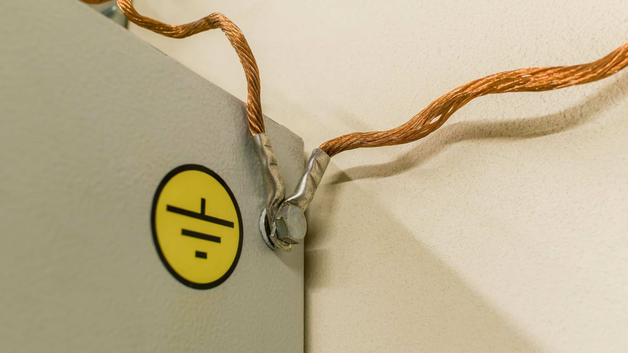 A copper multi-strand grounding wire screwed with a nut to a metal cabinet with a yellow "Grounding" label.