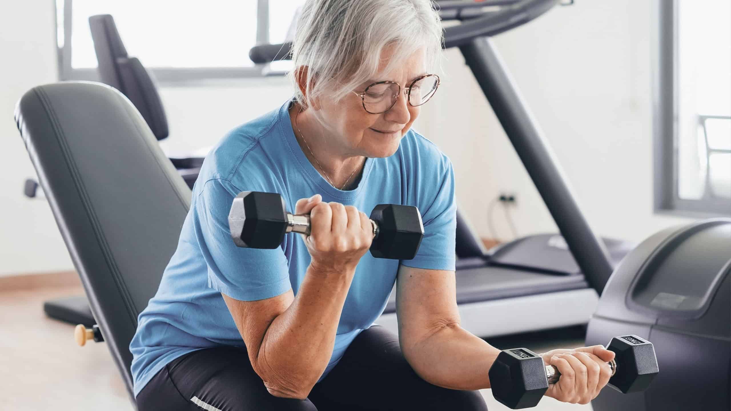 Smiling and active senior woman doing exercises with dumbbells in gym area. Sport, healthy lifestyle, gym, wellness concept