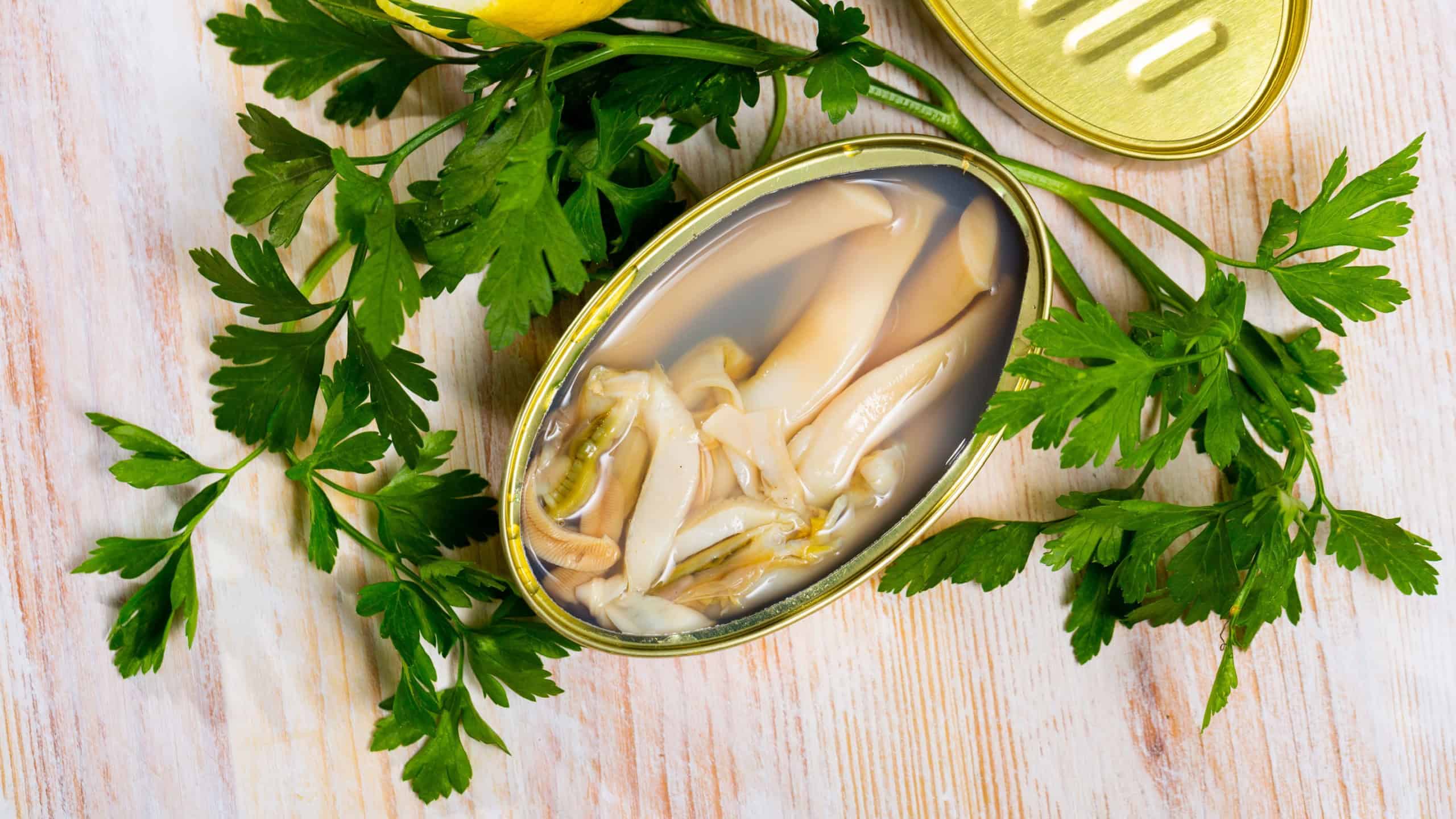 Seafood. Canned saltwater clams ensis in open tin can on wooden table with lemon and greens
