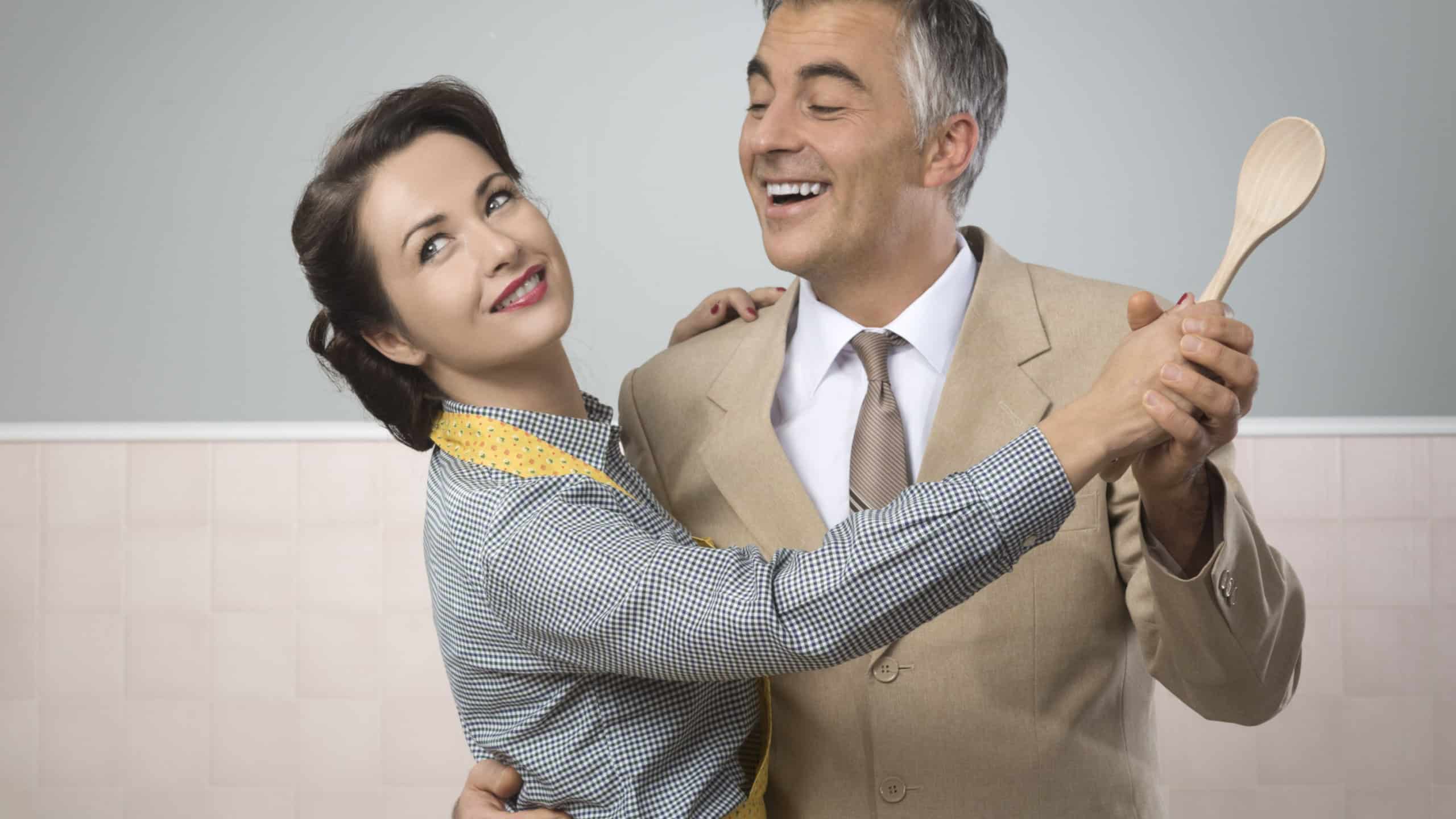 Smiling vintage couple dancing in the kitchen and holding a wooden spoon