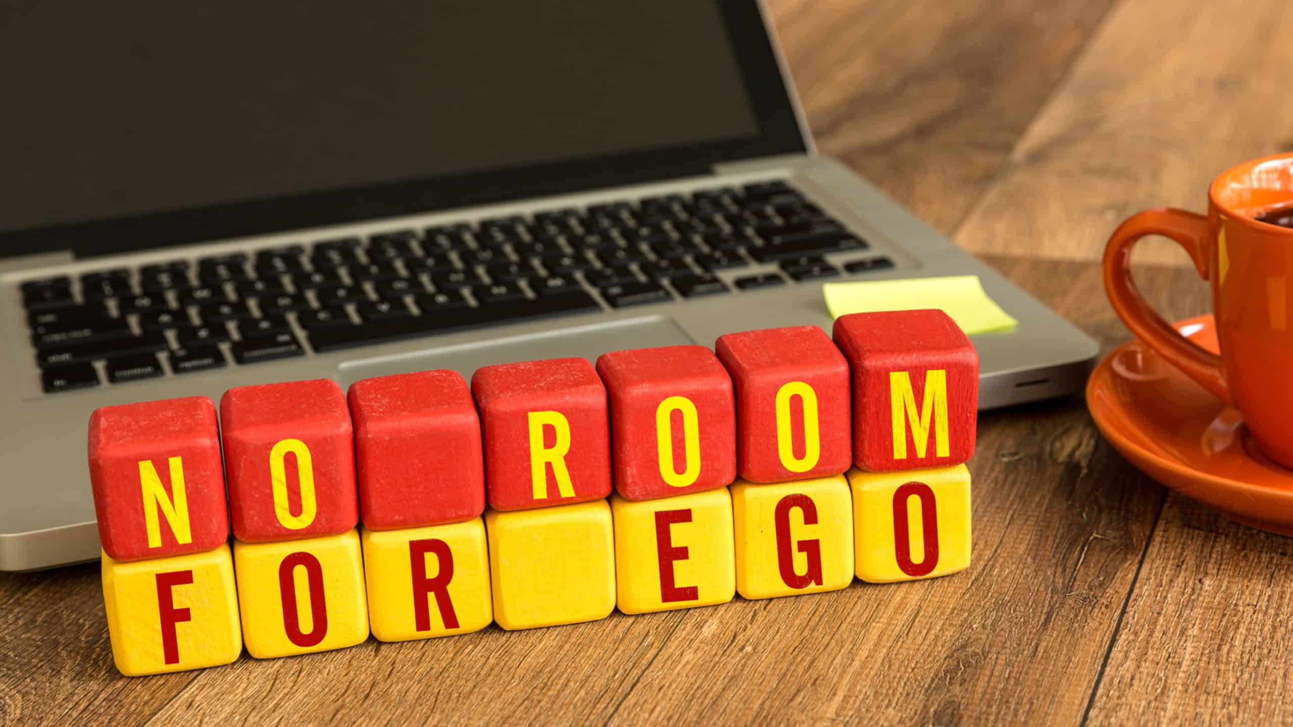 No Room For Ego written on a wooden cube in a office desk