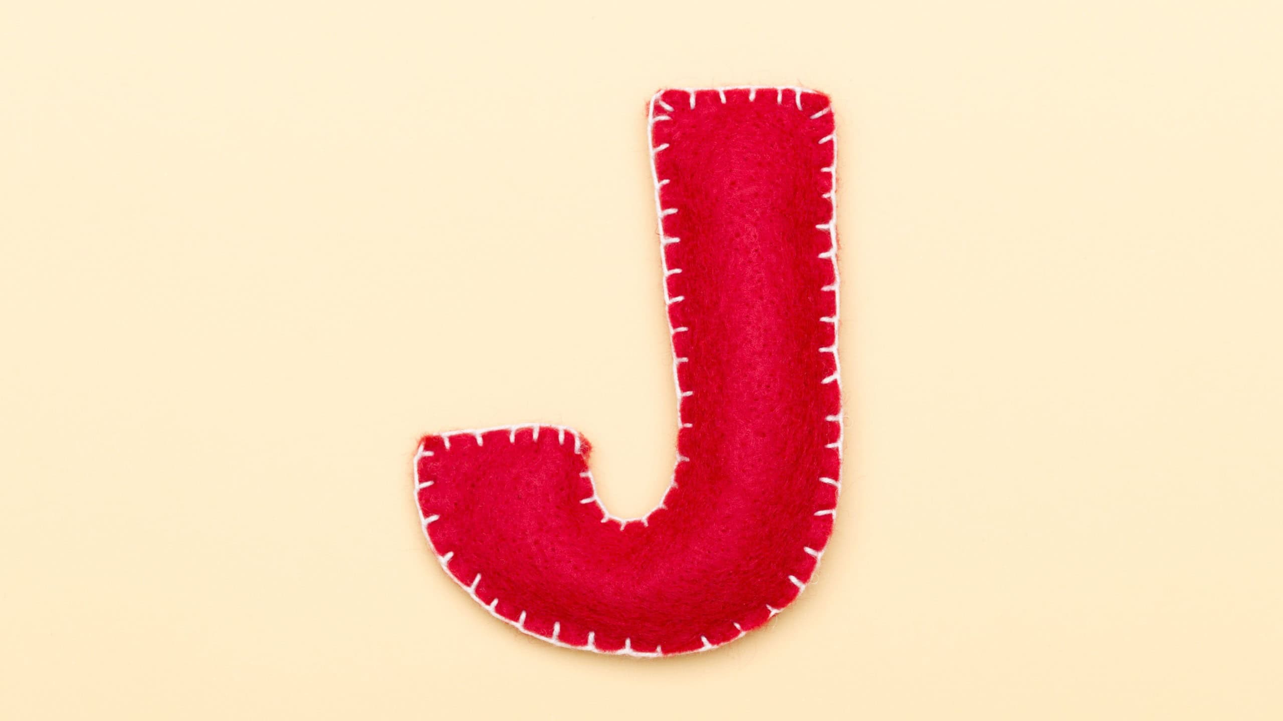 Letter of the alphabet J made of red felt isolated on Cream background.