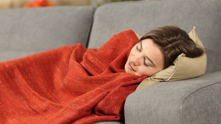 Portrait of a girl sleeping covered with an orange blanket lying on a comfortable couch in the living room at home