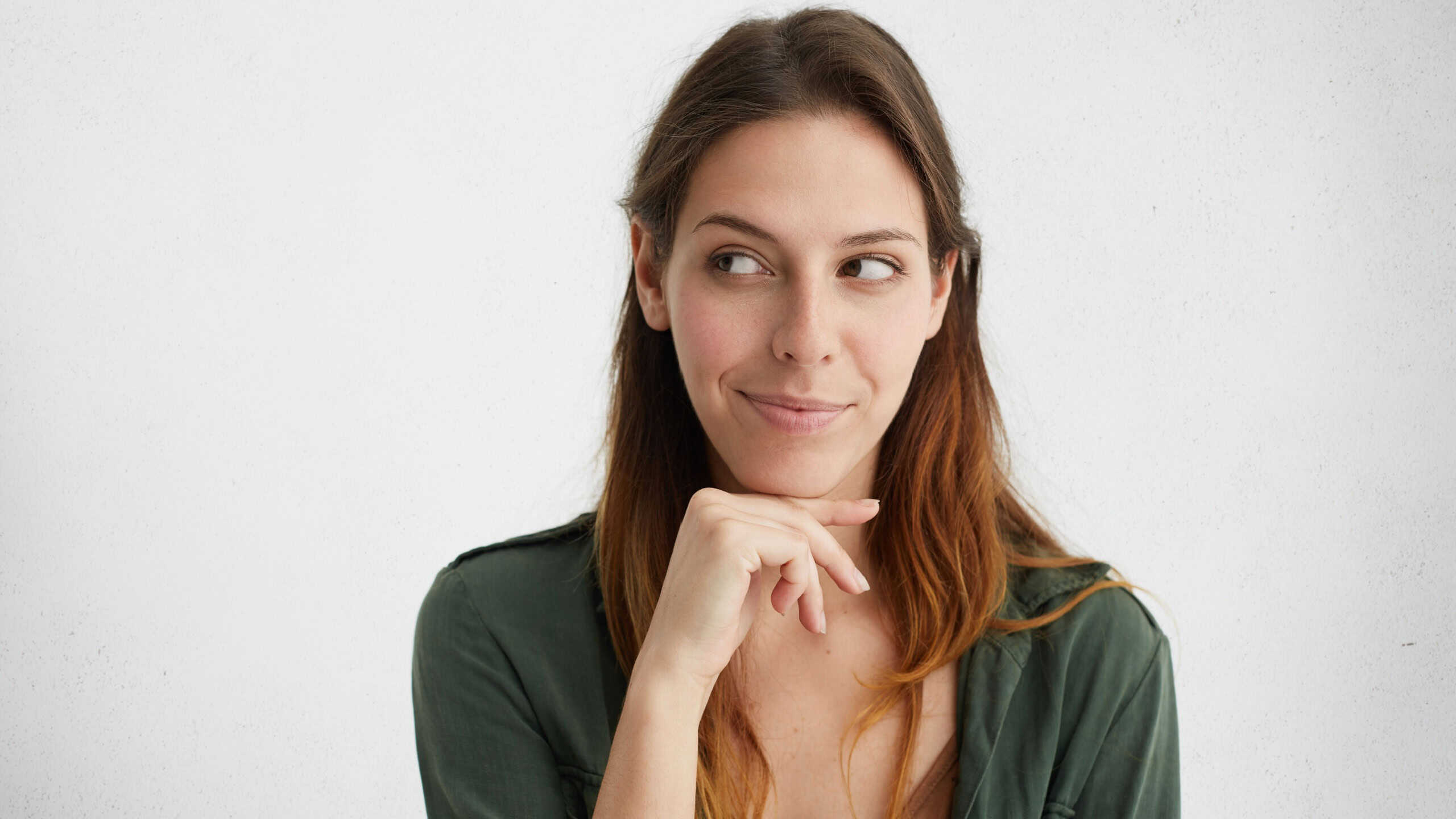 Headshot of cunning beautiful woman with straight dyed hair looking aside holding hand under chin indenting to realize tricky plan. Attractive female having sly expression while looking aside