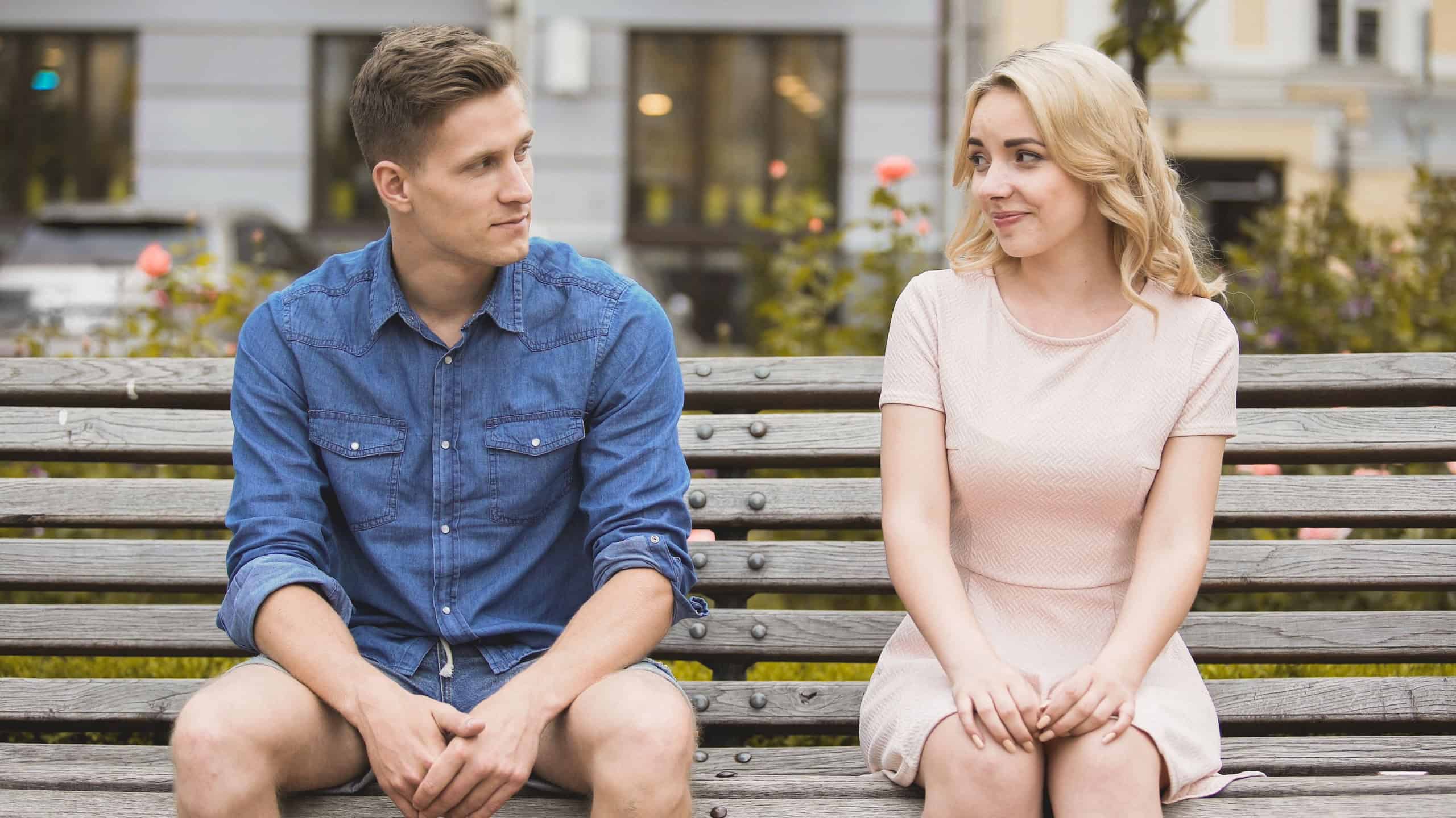 Couple sitting on bench and smiling at each other, reconciliation after fight