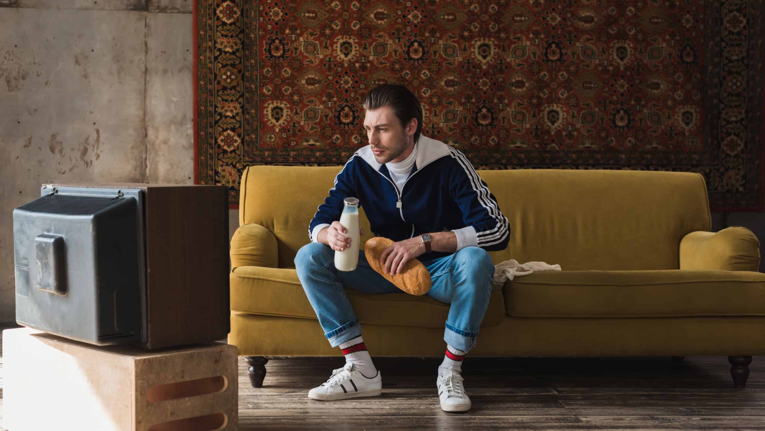 handsome young man in vintage clothes with bottle of milk and loaf of bread watching tv