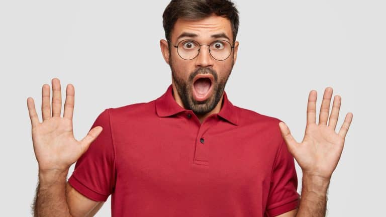 Mad man keeps palms in front, has shocked expression, opens mouth widely, has terrific look, exlaims he is not guilty, dressed in casual red t shirt stands over white background. Oh no, it cant be so!