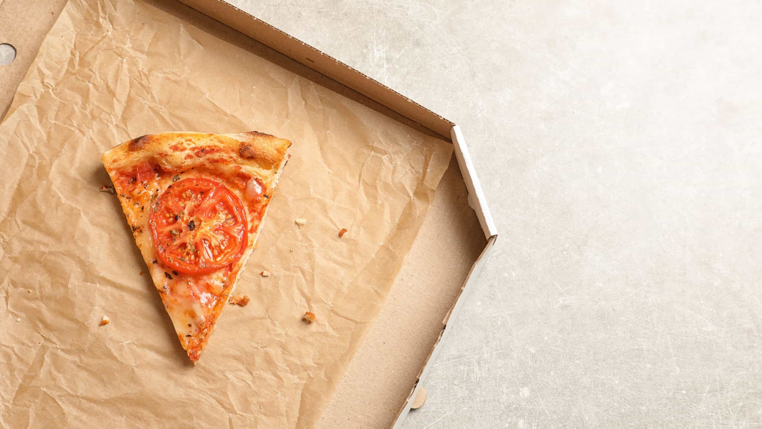 Last slice of cheese pizza in cardboard box on grey table