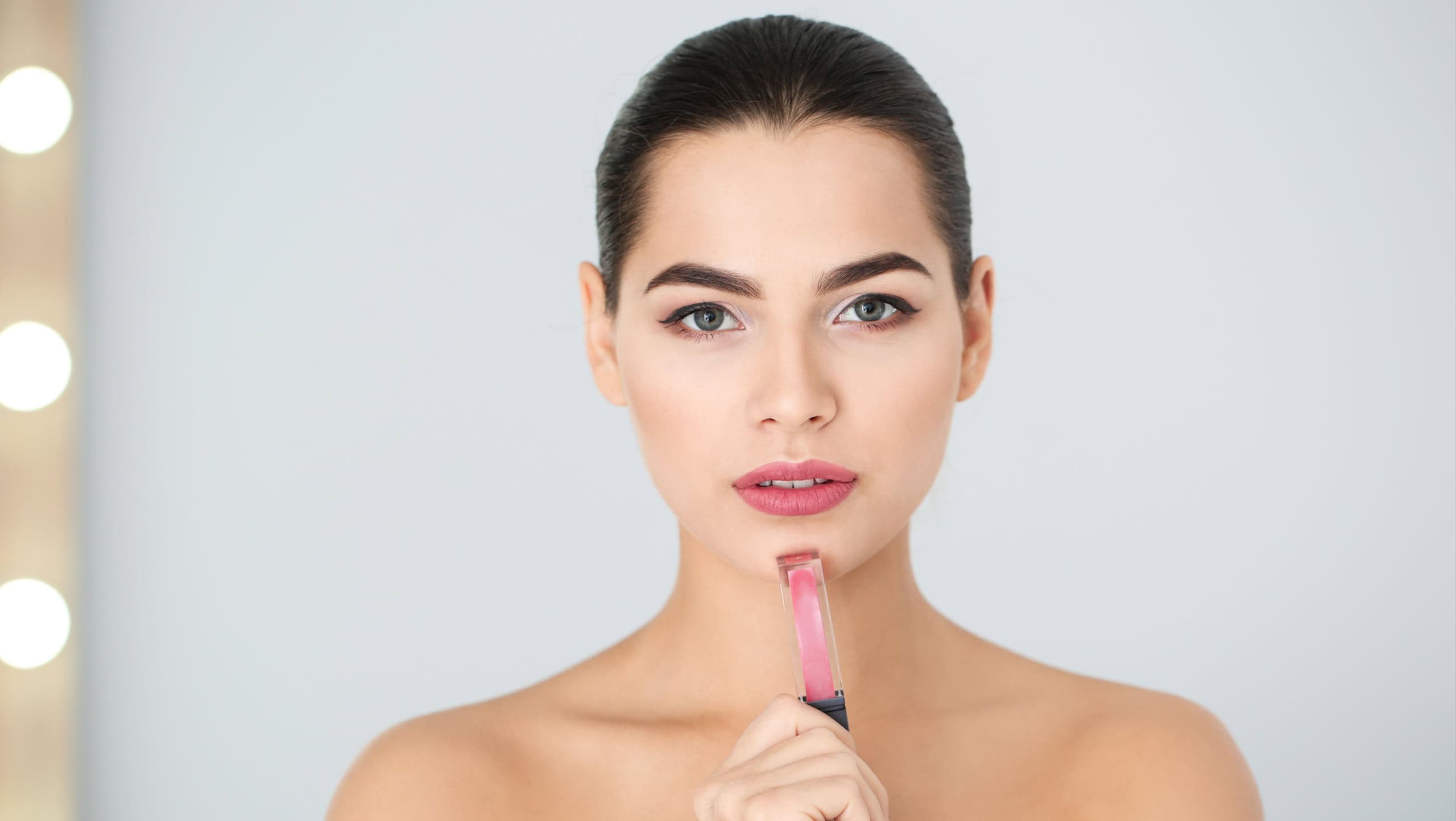 Young woman with liquid lipstick on blurred background