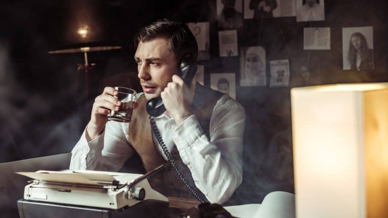 Detective talking on telephone and drinking cognac in office