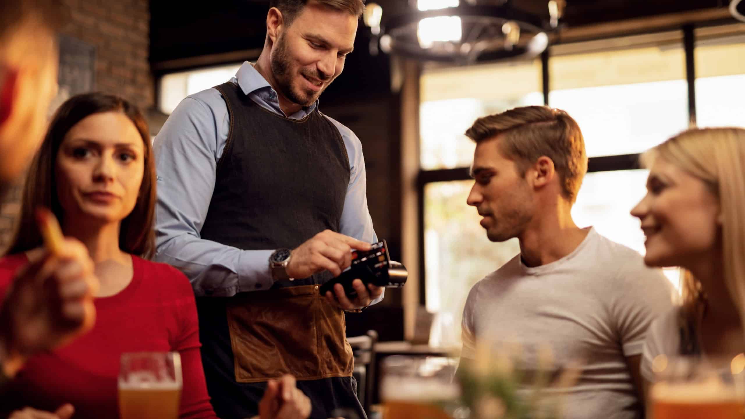 Young waiter accepting credit card payment from his guest who is paying restaurant bill.