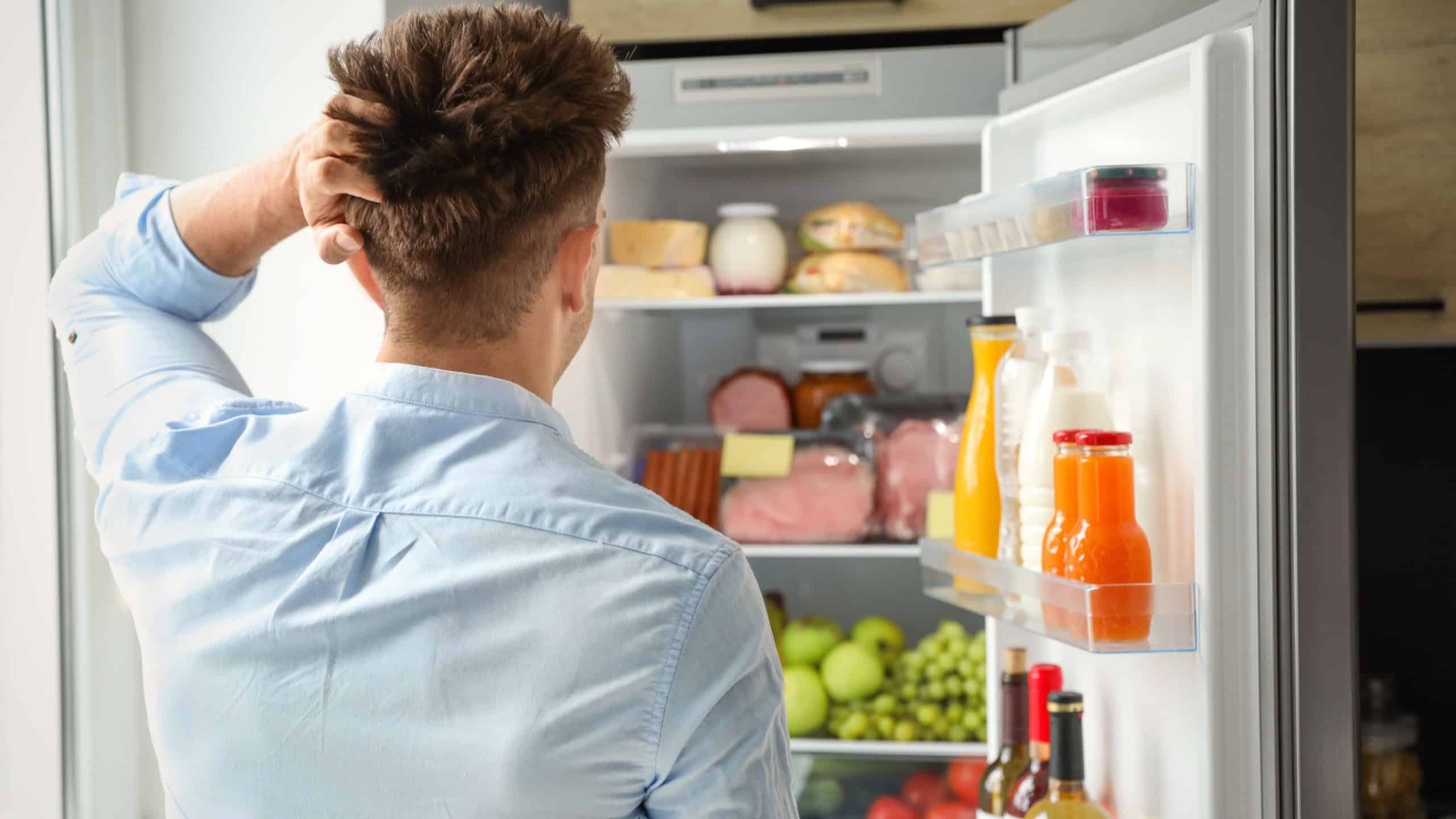 Man looking into refrigerator full of products in kitchen