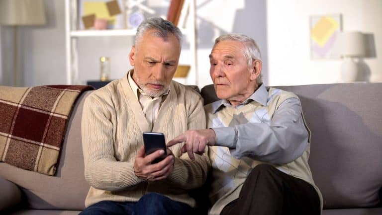 Two mature friends learning to use smartphone application, modern technology
