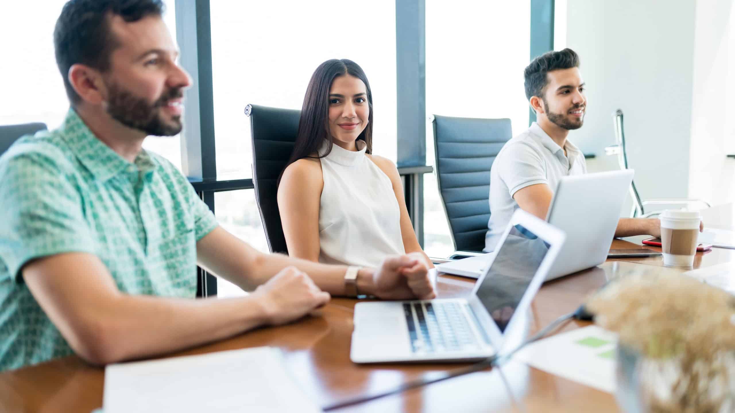 Beautiful young businesswoman making eye contact while sitting amidst colleagues at desk during meeting in office
