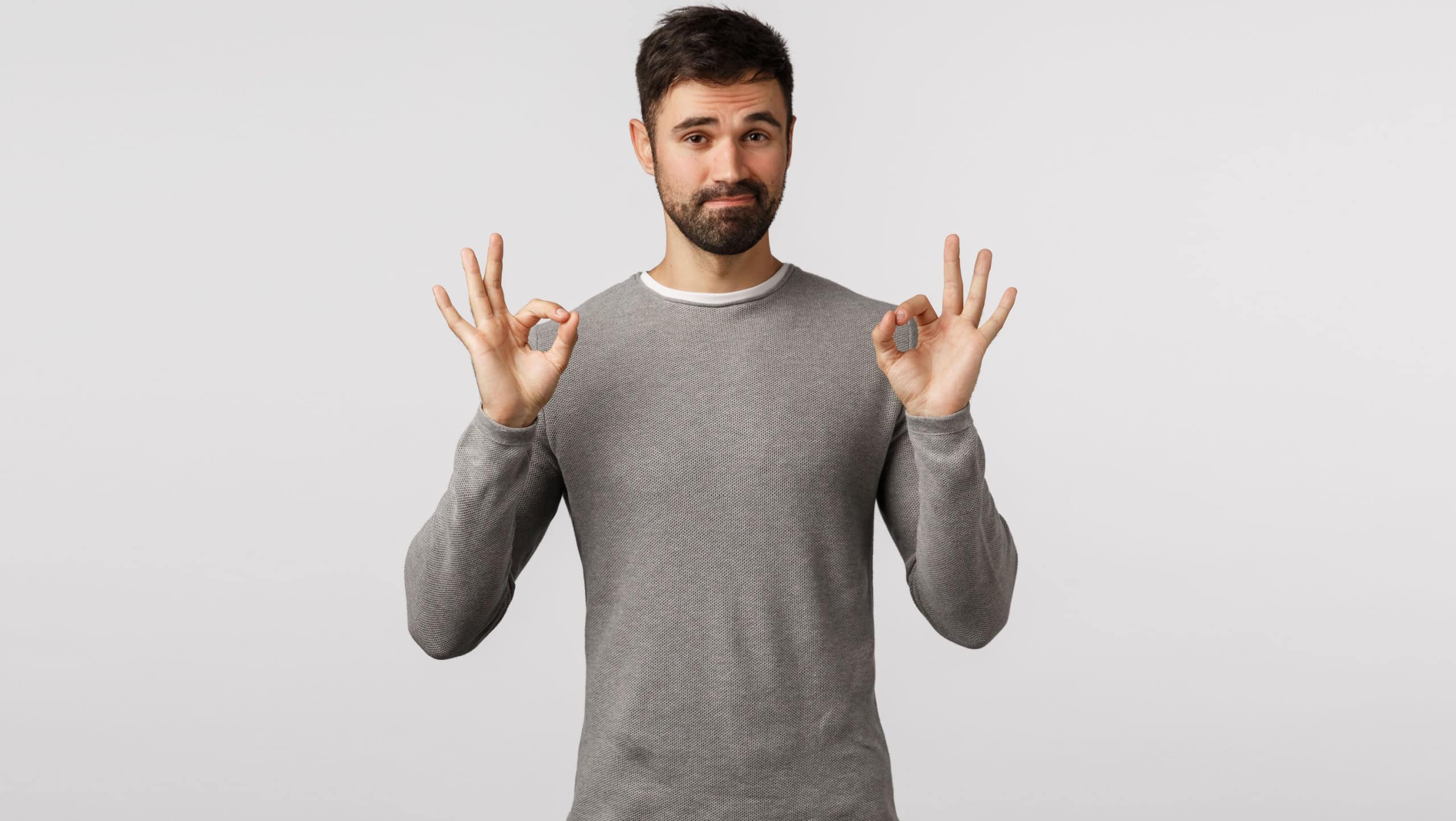 Not bad, well done. Pleased judgemental adult bearded husband in grey sweater agree with you, show okay, ok confirmation gesture and smiling, rate normal product, recommend, stand white background
