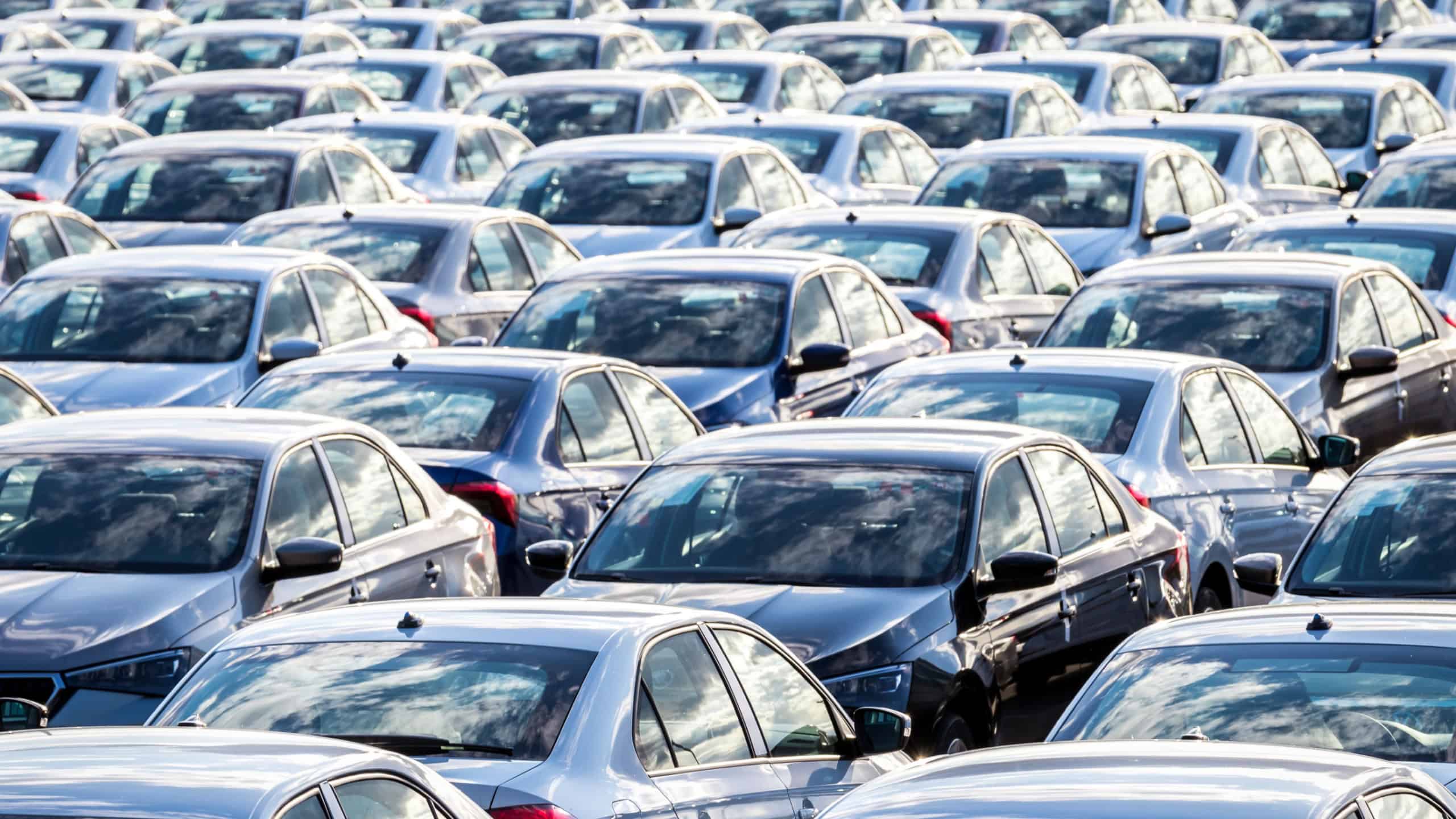 Rows of a new cars parked in a distribution center on a car factory on a sunny day. Parking in the open air.