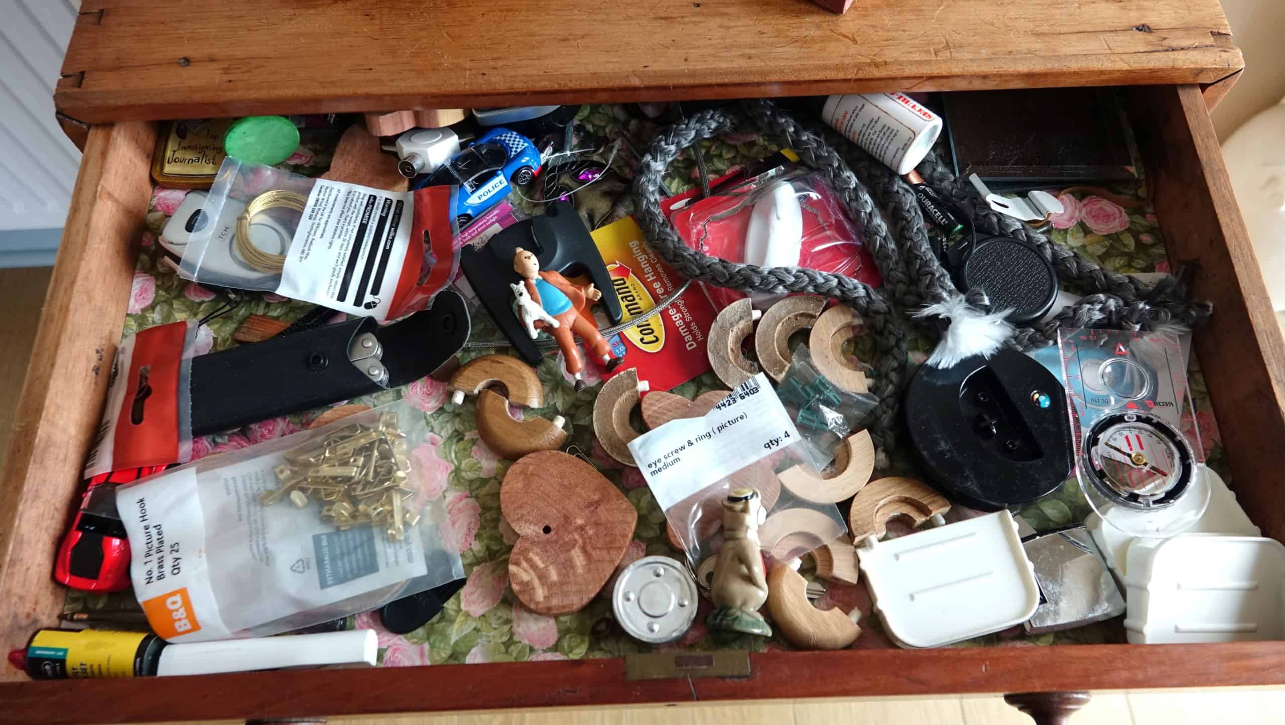Dartmoor England. Looking inside a domestic drawer with a large jumble of small rarely used articles including, compass, picture hooks, Tin Tin and dog model, decorative rope, knife, film.