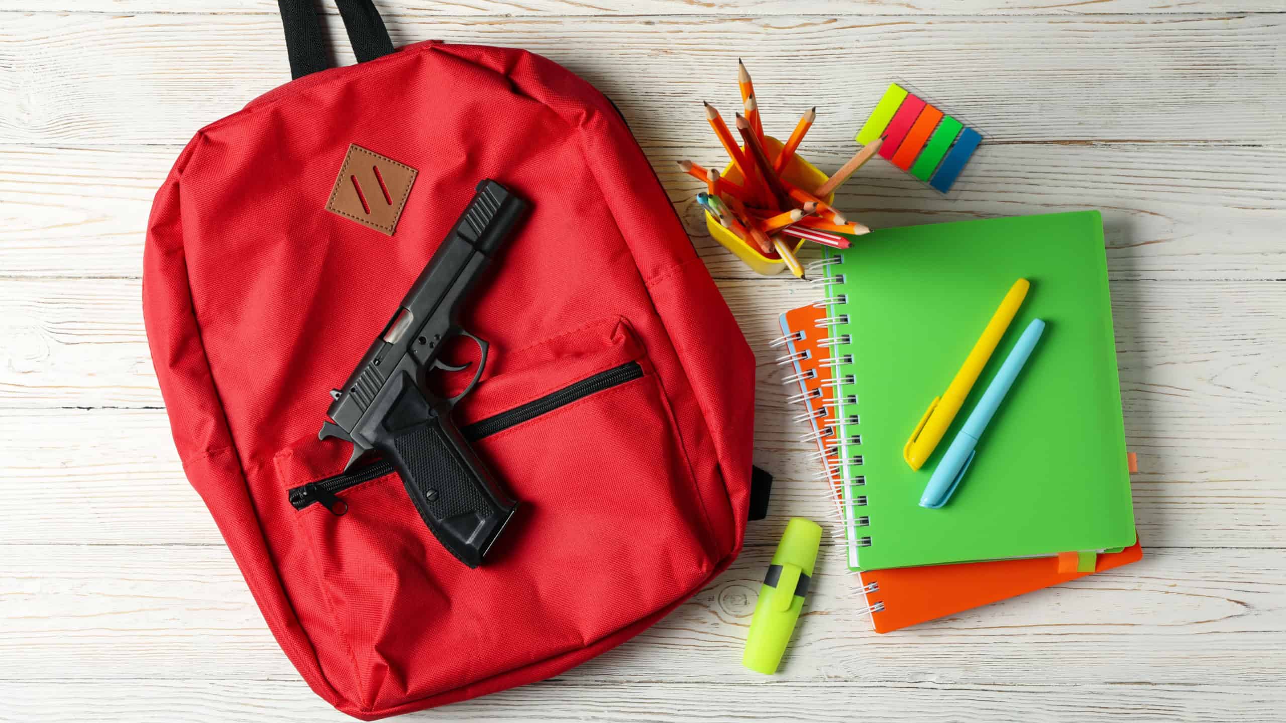 School accessories and gun on white wooden table. School violence