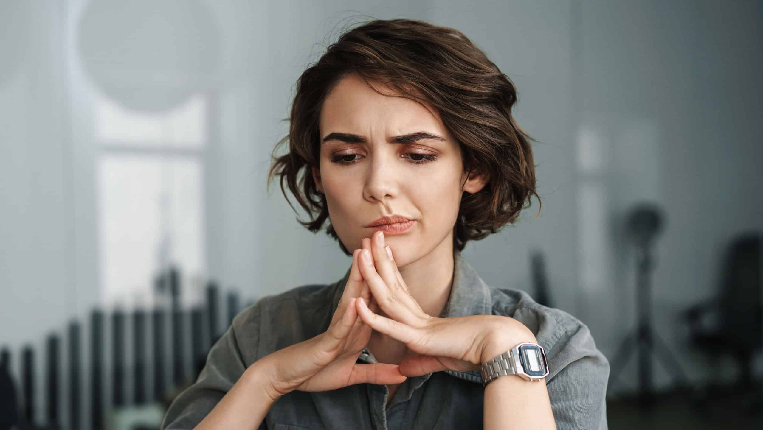 Image of young beautiful brooding woman working with laptop while sitting at table in office