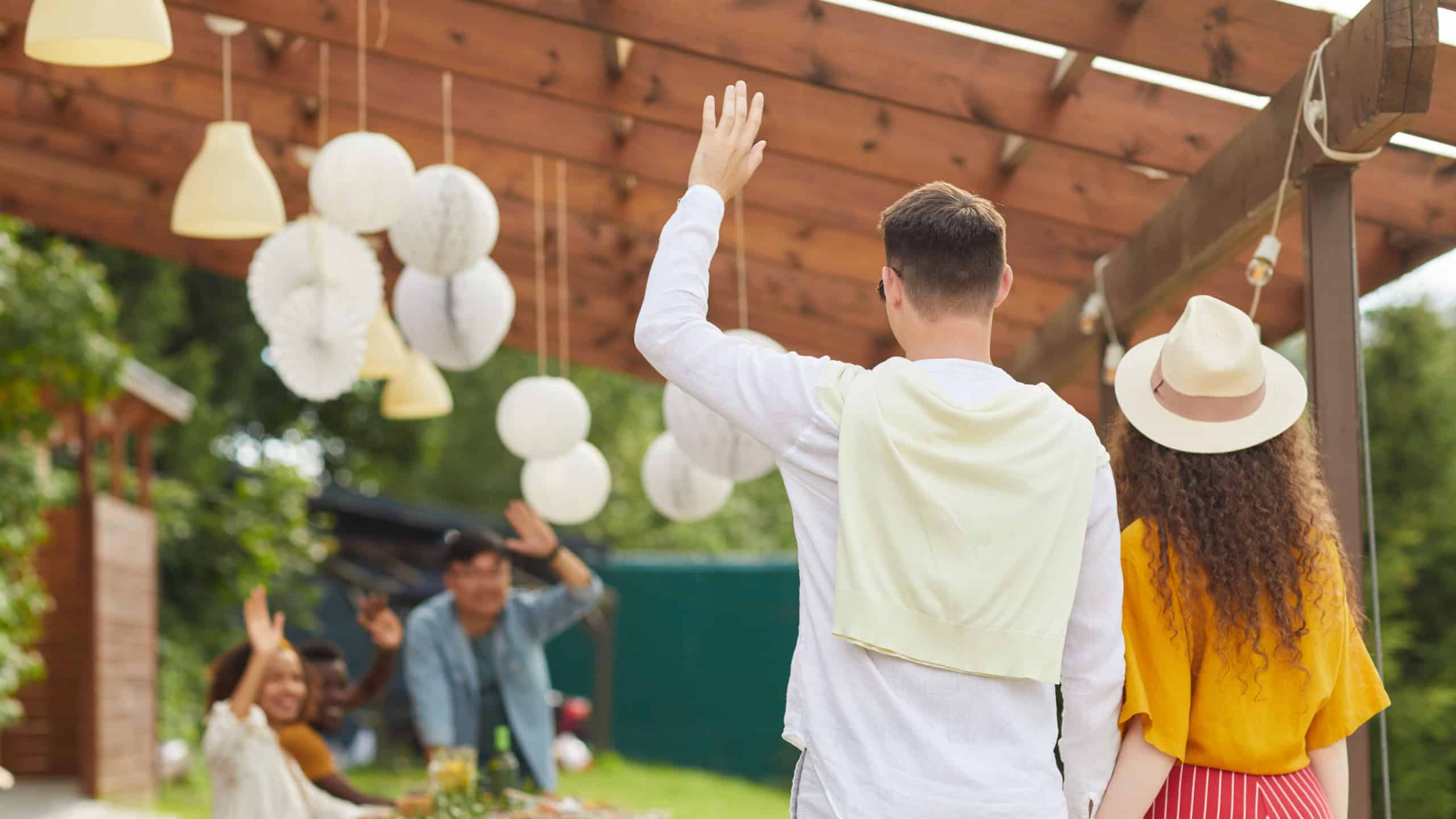 Back view portrait of young couple waving to friends while leaving outdoor party in Summer