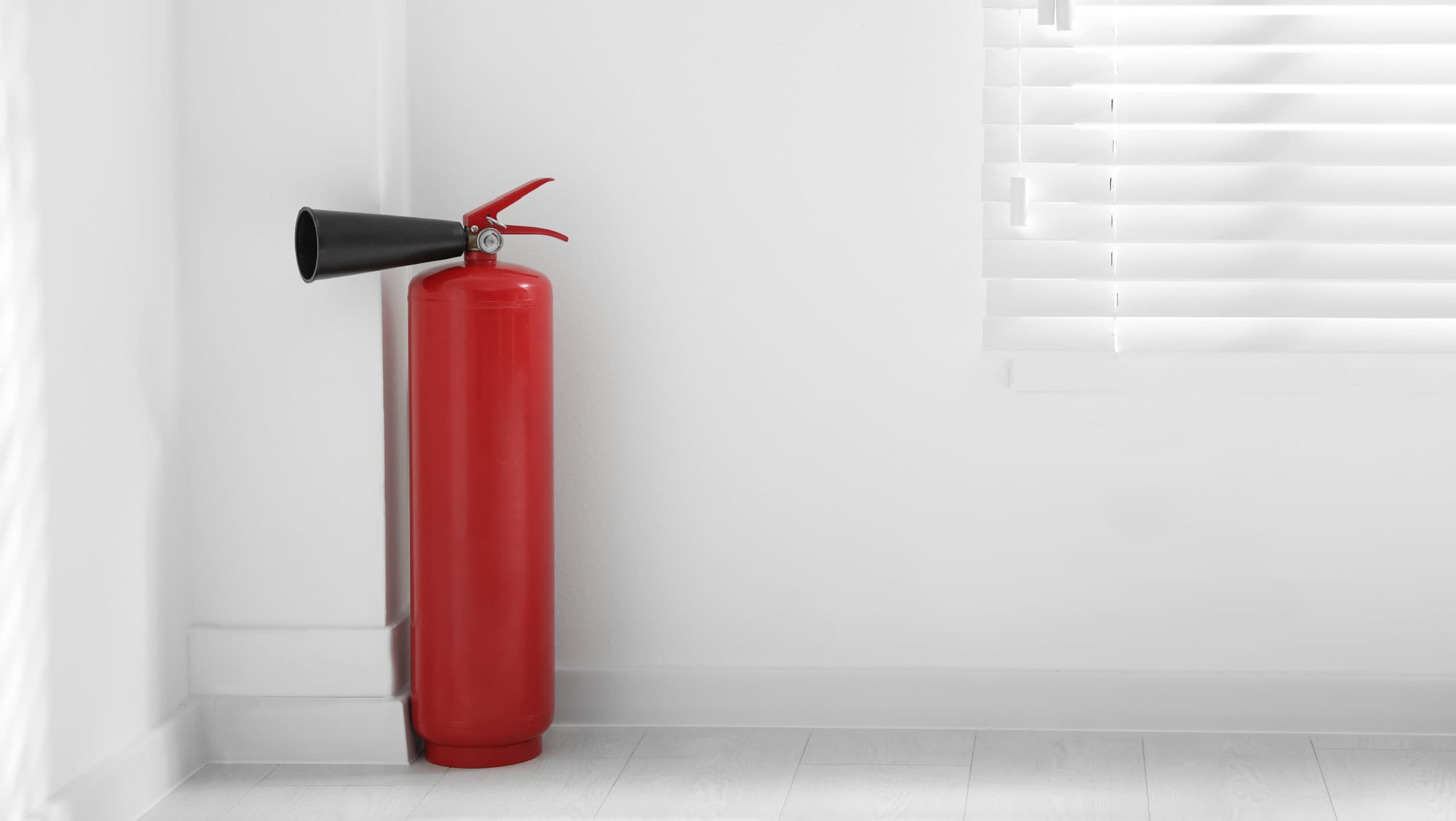 Fire extinguisher near white wall indoors. Space for text