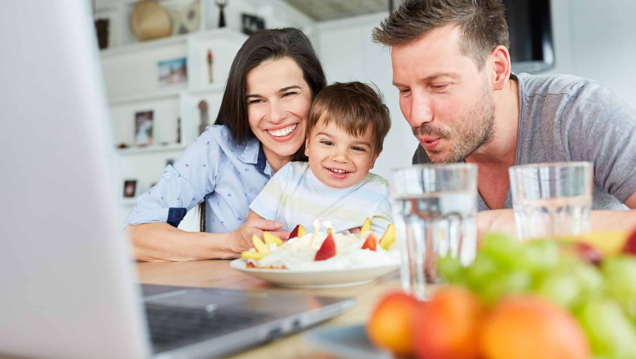 Family with child blows out candles on the cake in video chat for a birthday