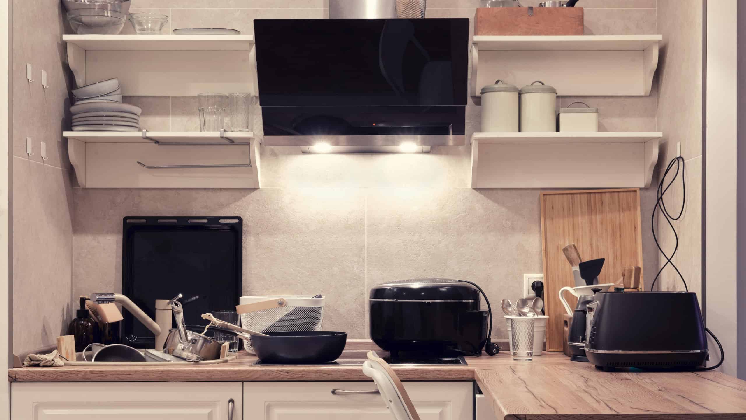 The kitchen is cluttered with dishes, appliances and items. Dirty plates and pans in the kitchen sink