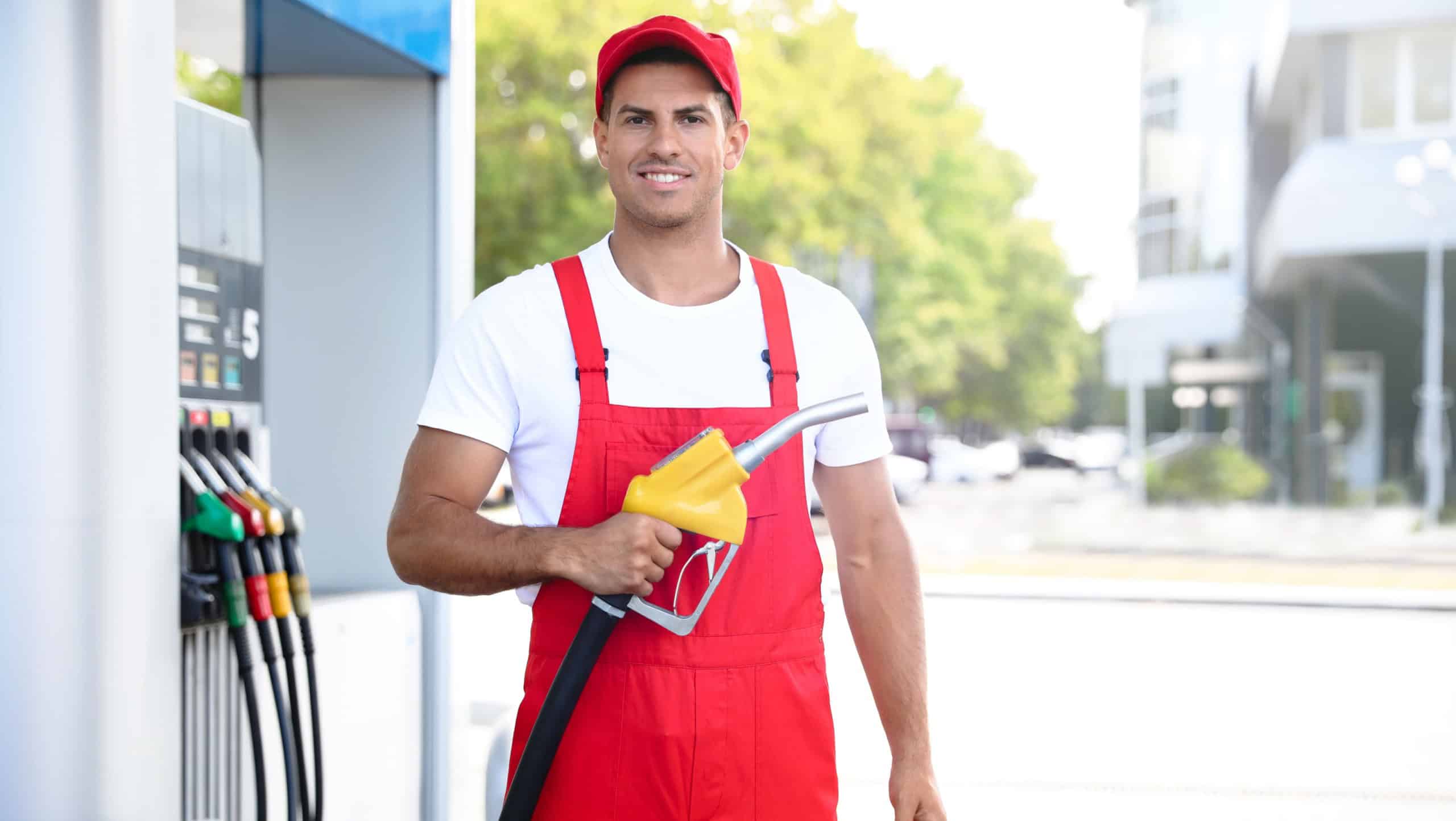 Worker with fuel pump nozzle at modern gas station