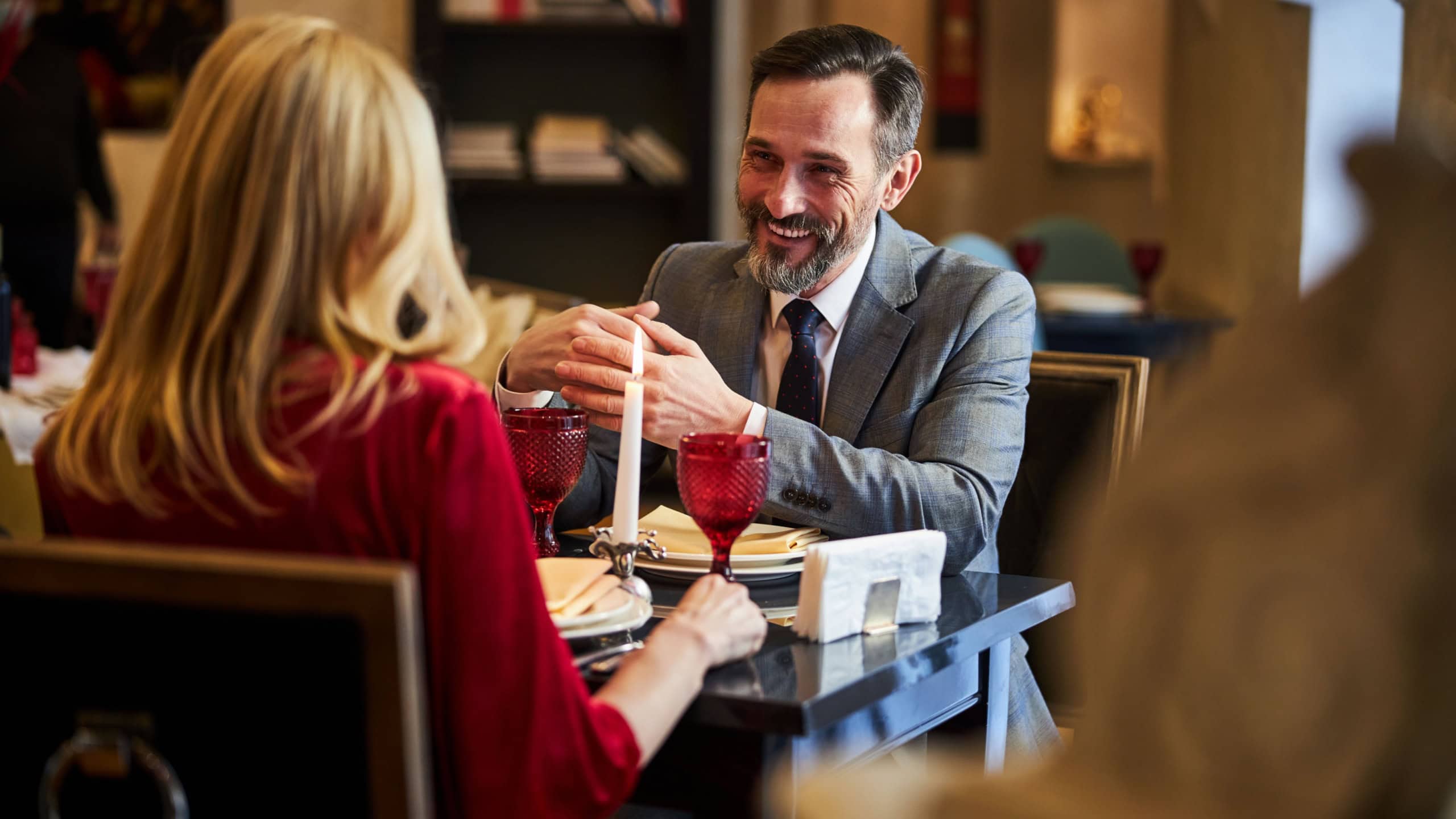 Cheerful man in a suit smiling while sitting at dinner table with a blonde lady