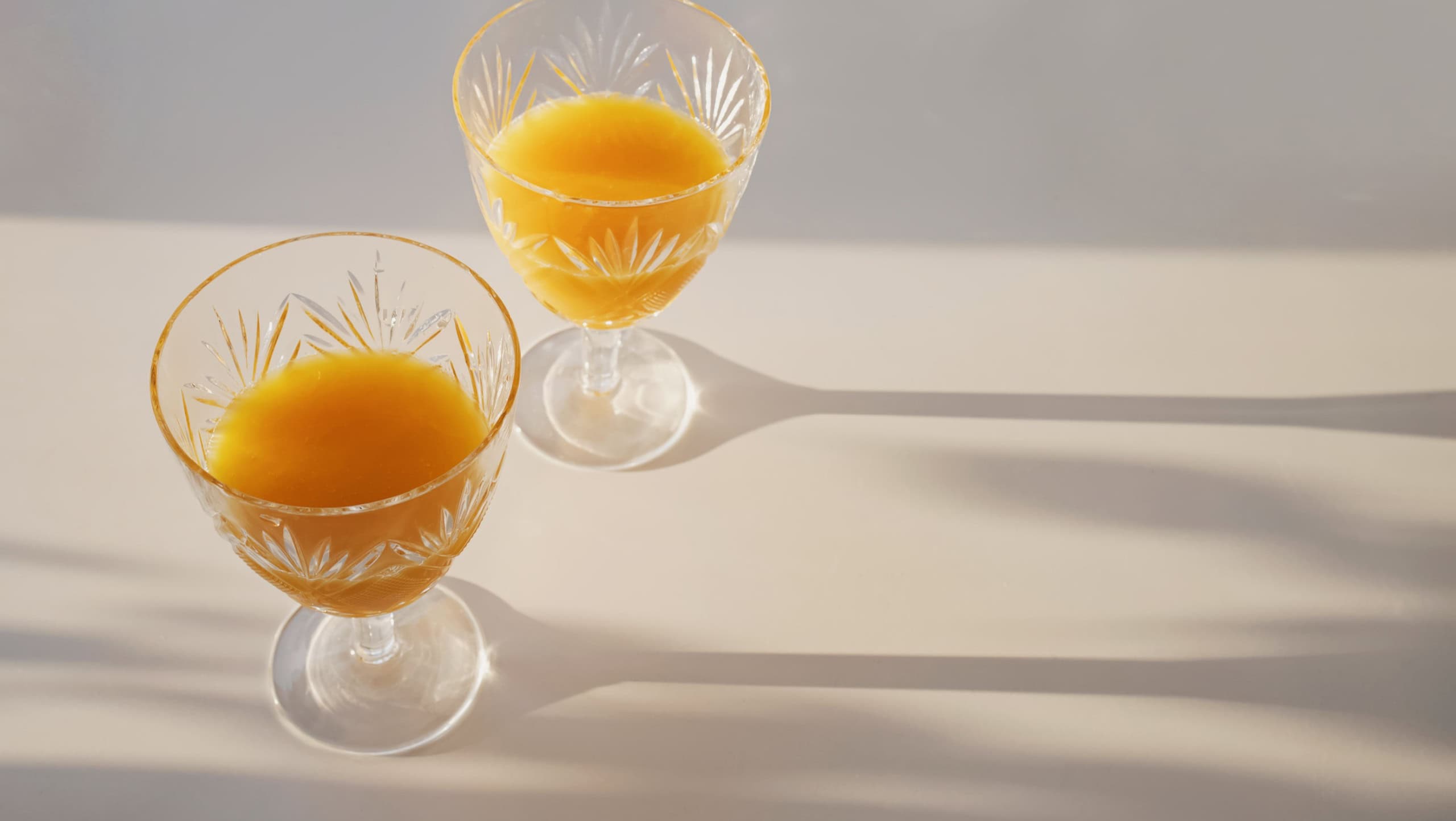 Luxury vintage crystal glass with frech orange juice on the white table with long shadows. Natural sunlight, minimal food concept