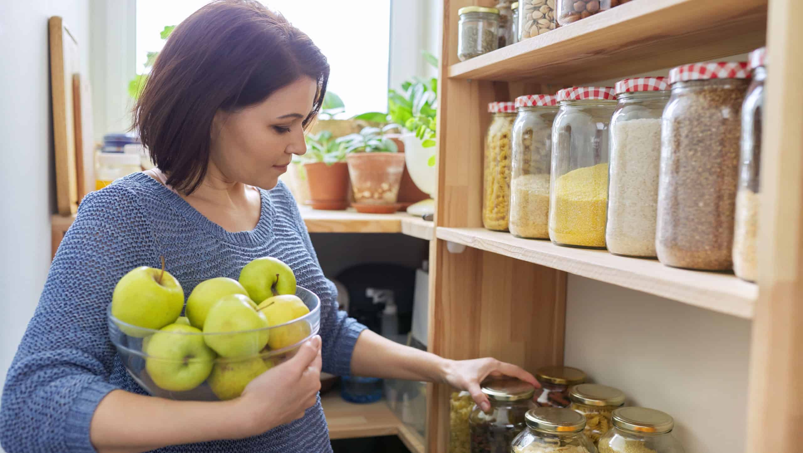 Woman with bowl of green apples in pantry, organizing in kitchen