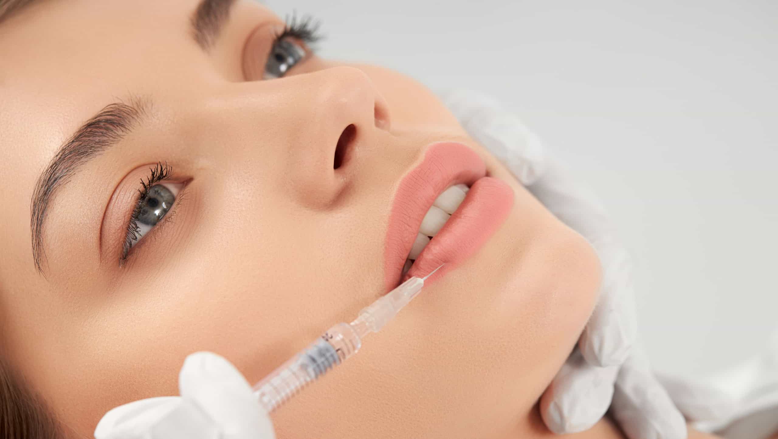 Close up portrait of attractive young woman on procedure injection in lip with special preparation. Concept of process procedure lip augmentation in professional salon.