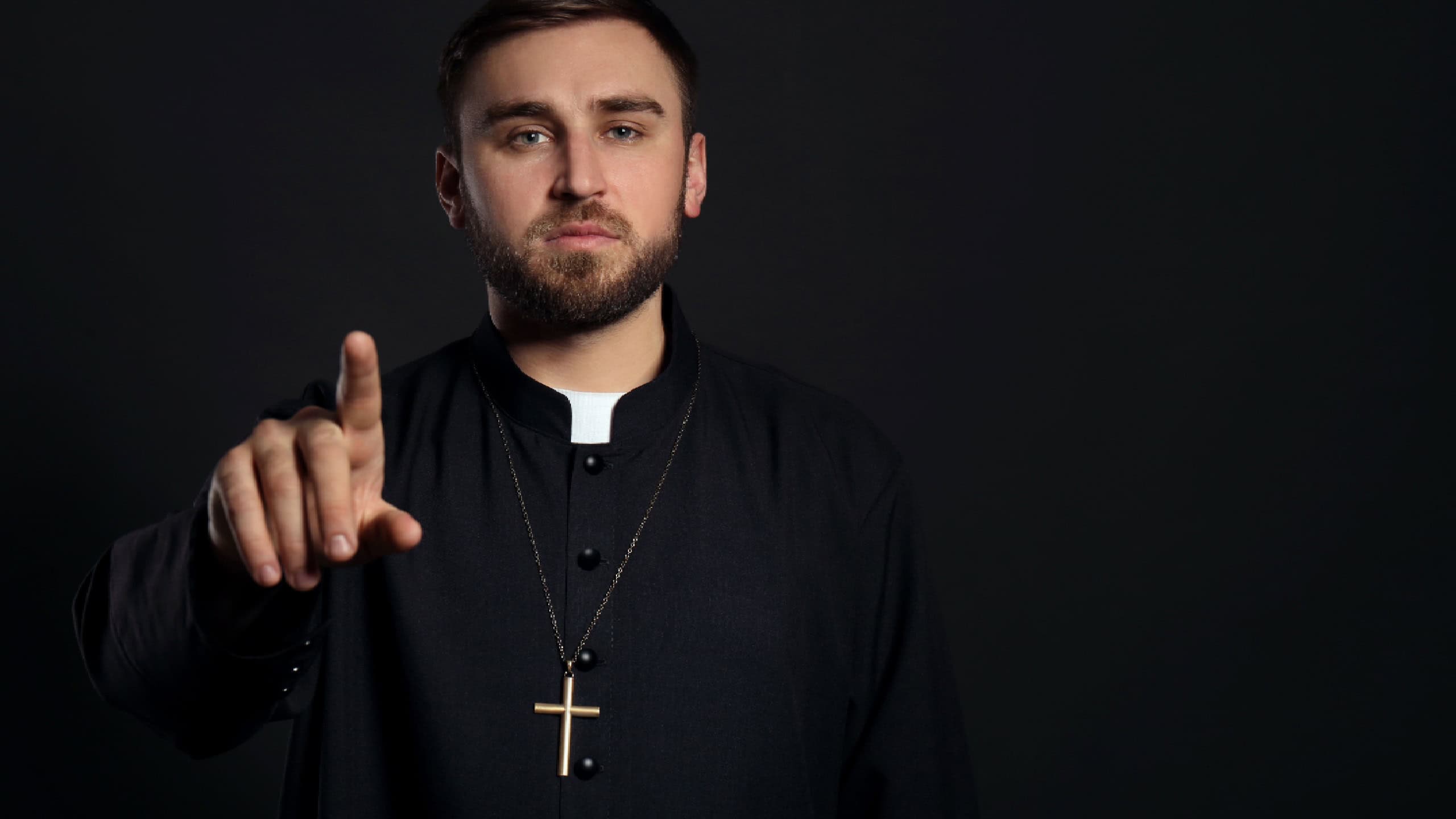 Priest wearing cassock with clerical collar on black background.
